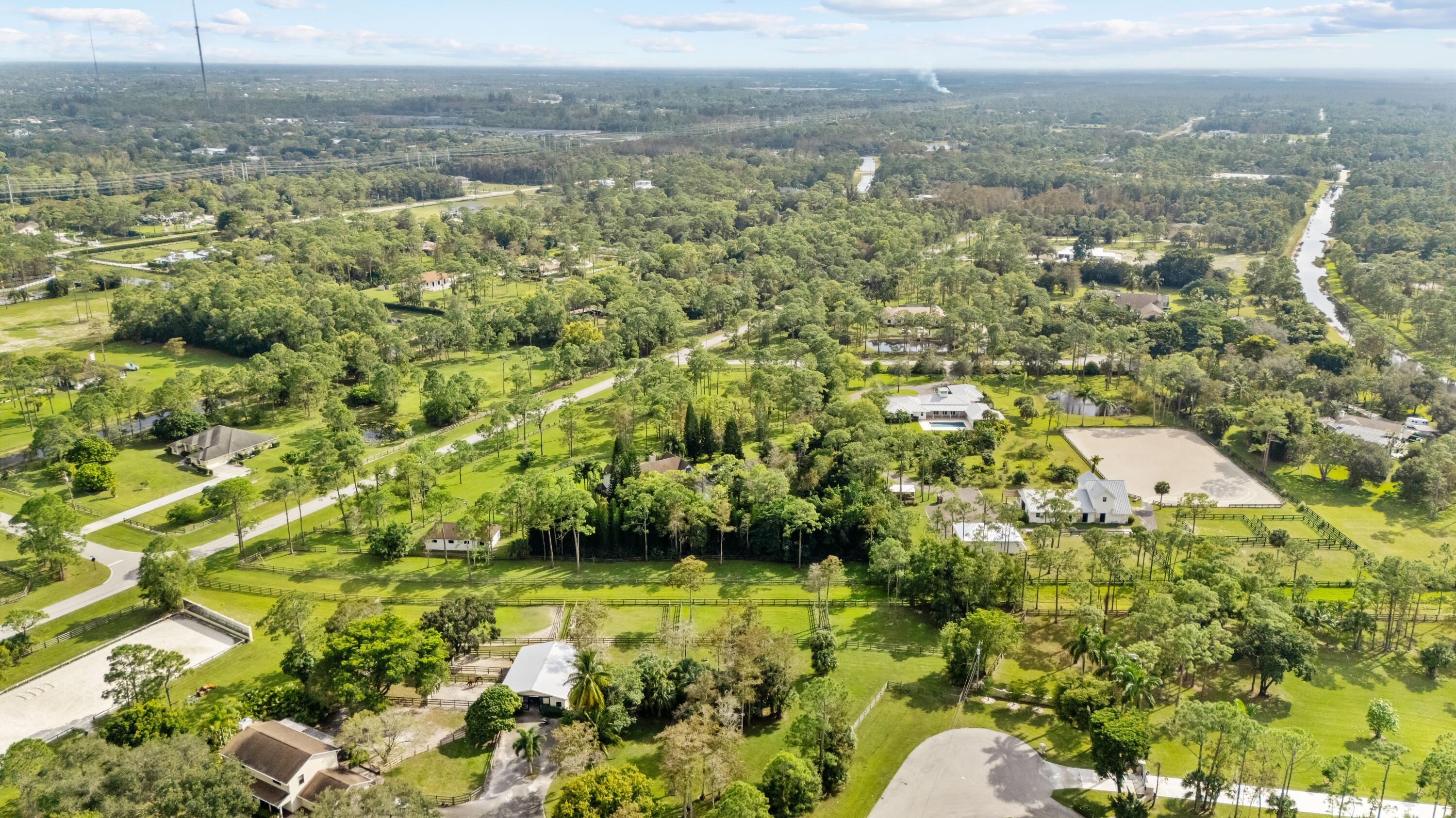Aerial view of equestrian acreage with fenced paddocks, riding arenas, and a canal nearby.