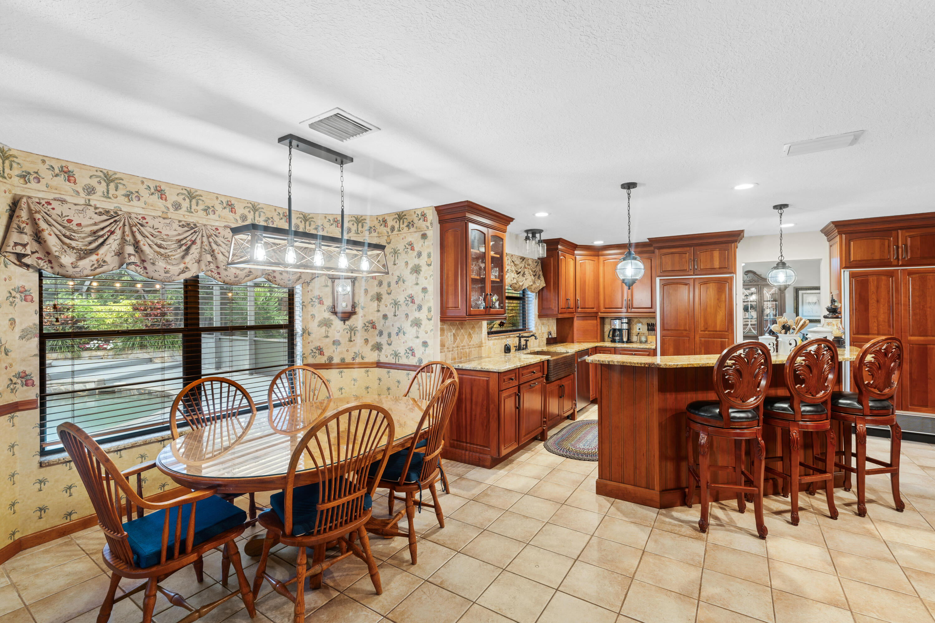 Kitchen and dining area with a wood island, carved bar stools, and a glass dining table by wide windows.