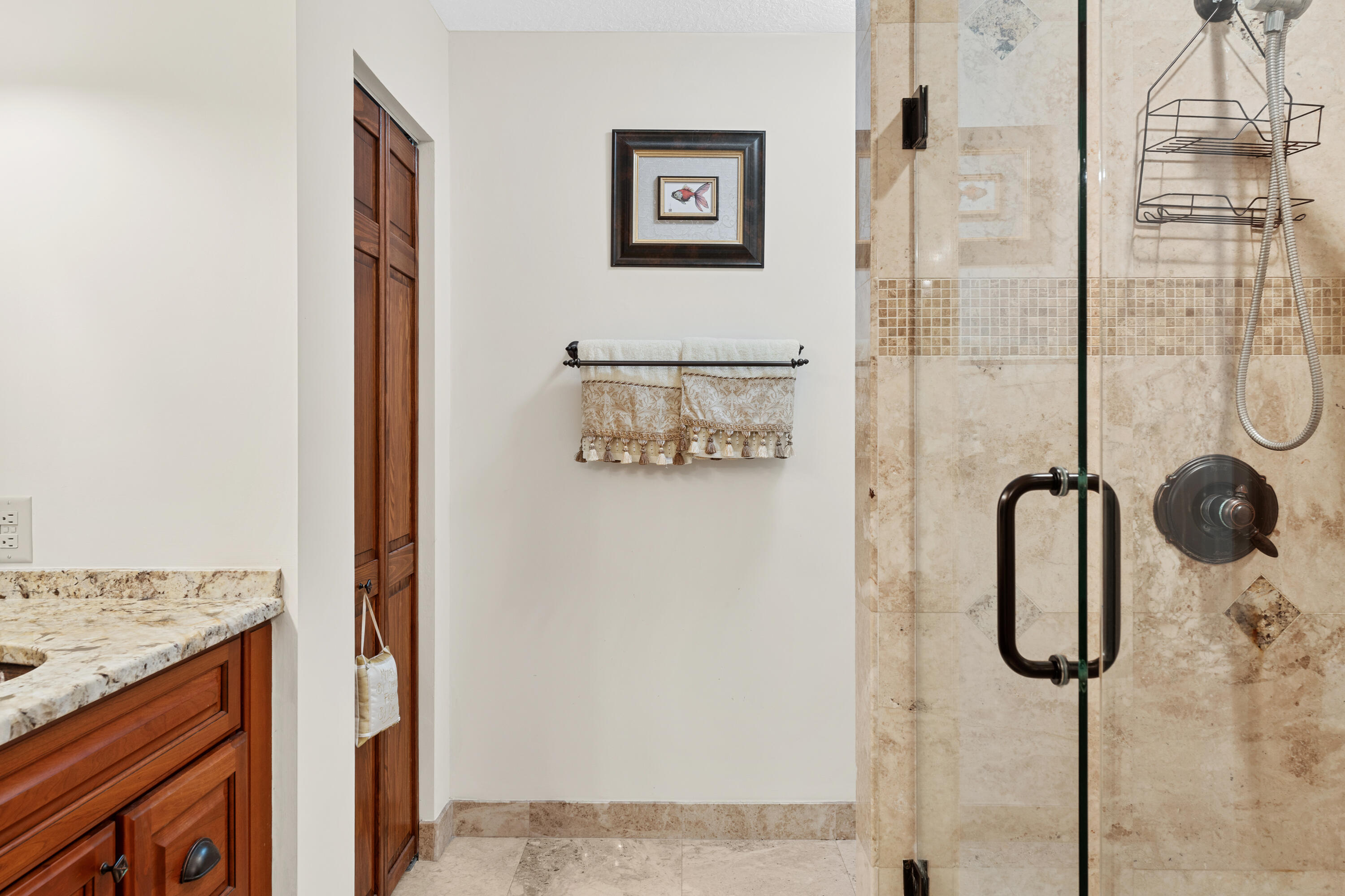 Bathroom with a glass shower, beige stone tile, and dark wood vanity.