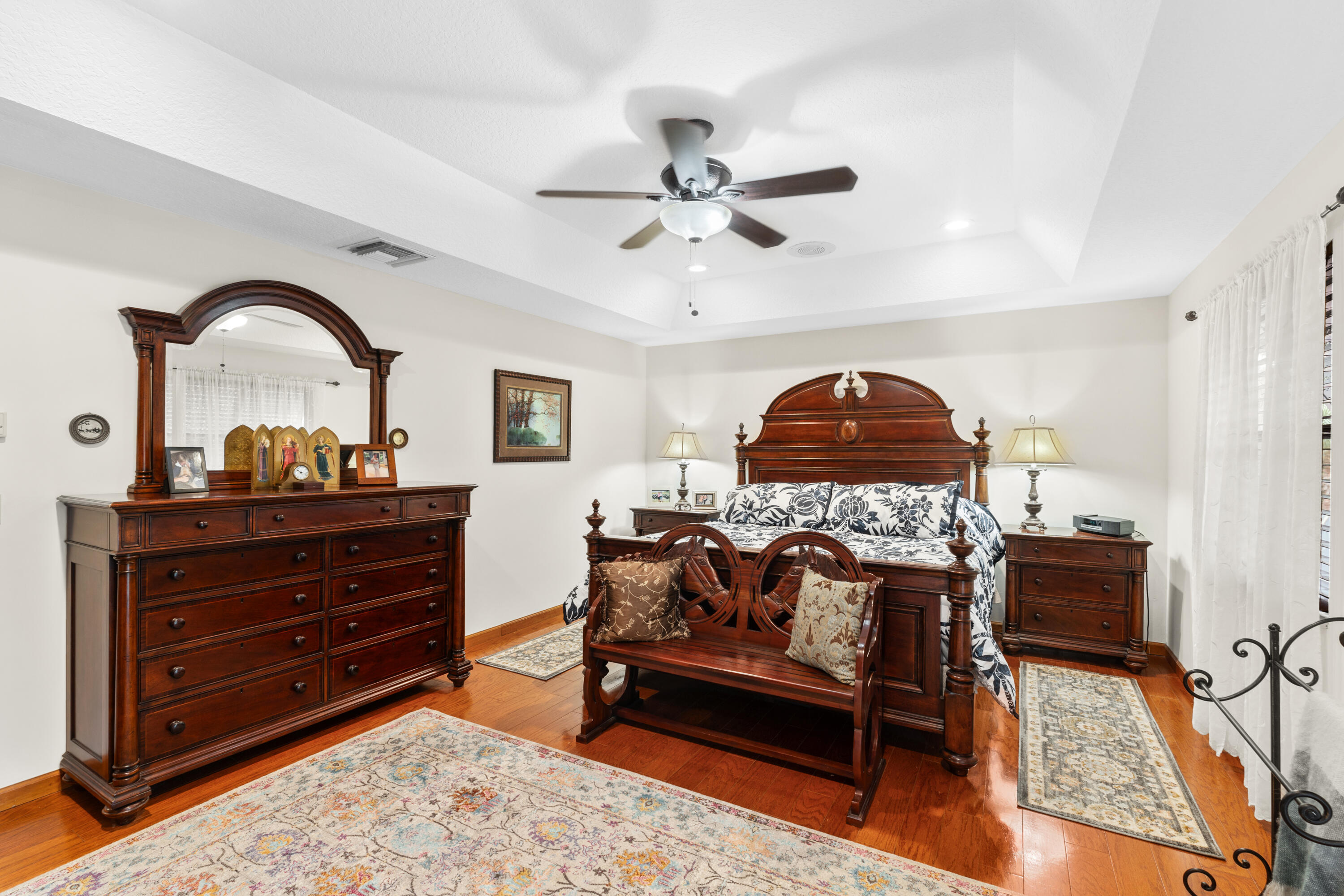 Bedroom with ornate dark wood furniture, a carved bed, patterned rugs, and polished hardwood floors.