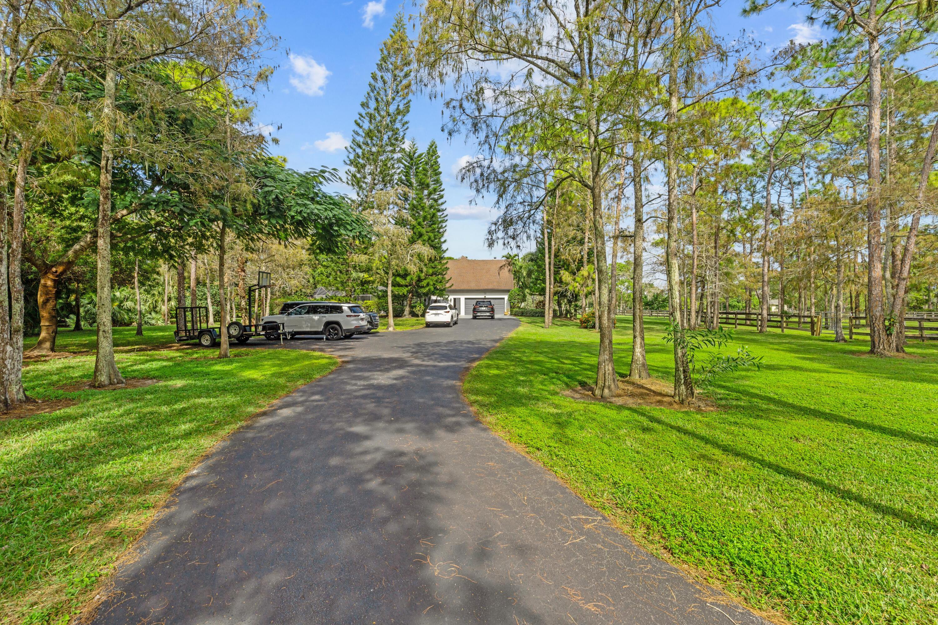 Tree-lined driveway leads to a detached garage, with fenced grounds and parked vehicles.