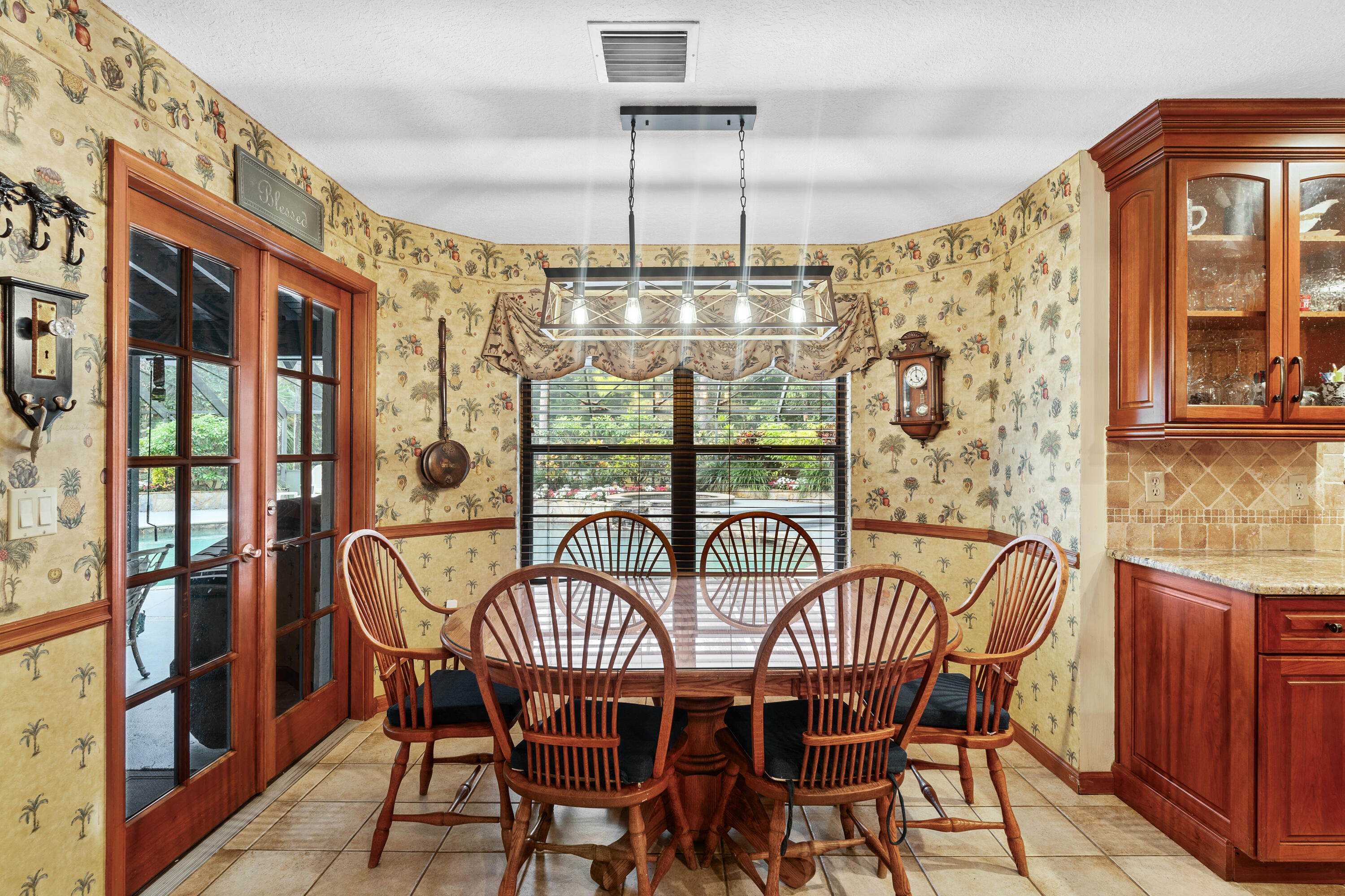 Dining area with a wooden table, spindle-back chairs, patterned wallpaper, and French doors to a patio.