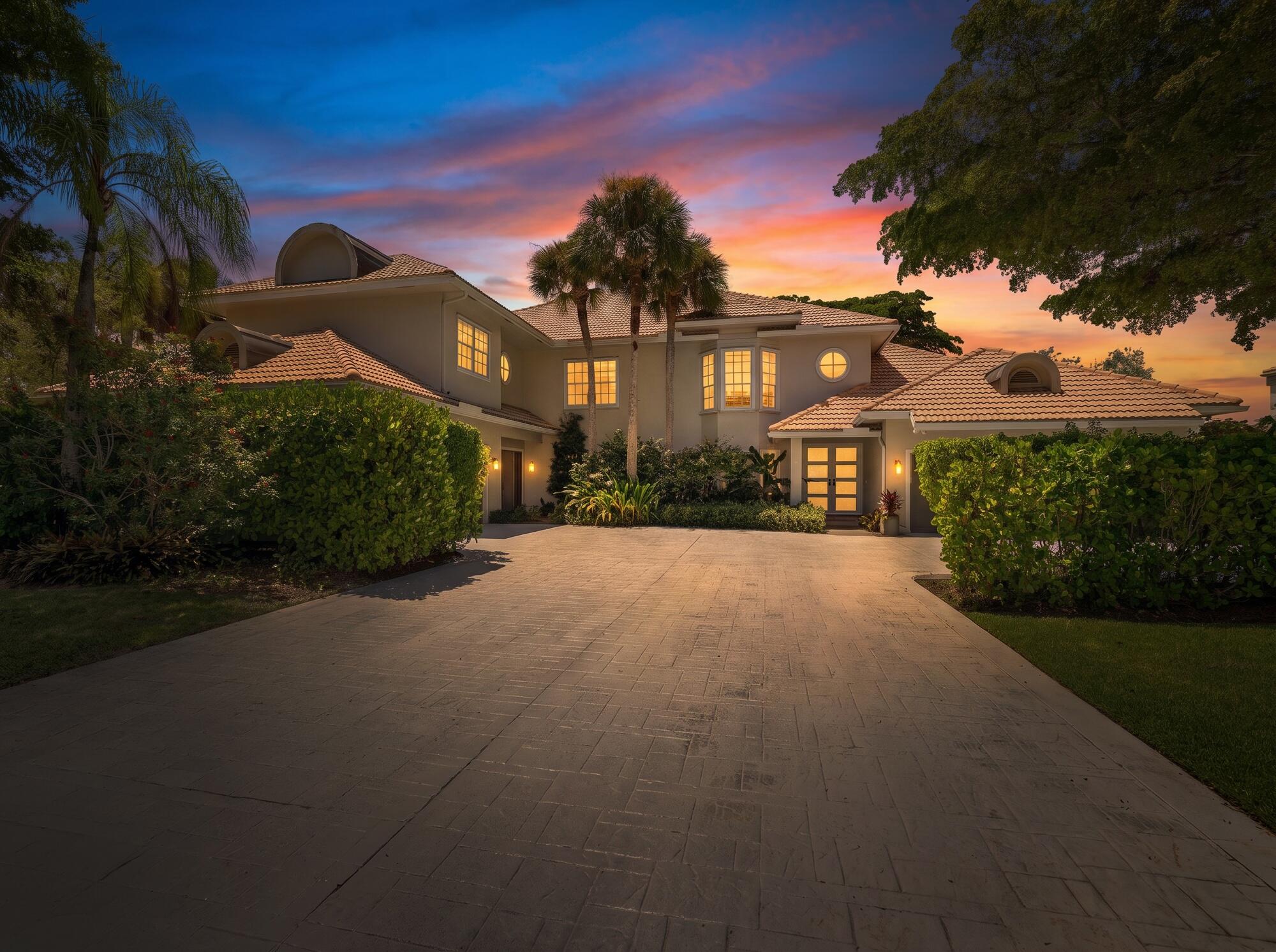 Two-story home with tiled roofs and a wide paved driveway at dusk.