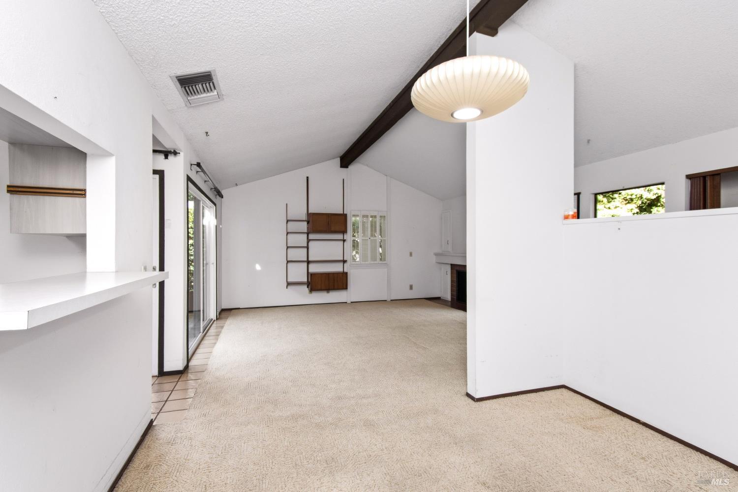 Vacant living room with vaulted ceiling, built-in shelving and a fireplace.