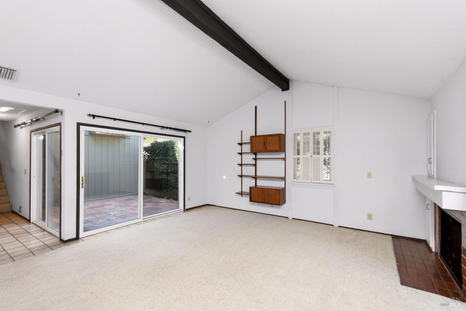 Living room with built-in wood shelving, a dark ceiling beam, and sliding glass doors to a patio.