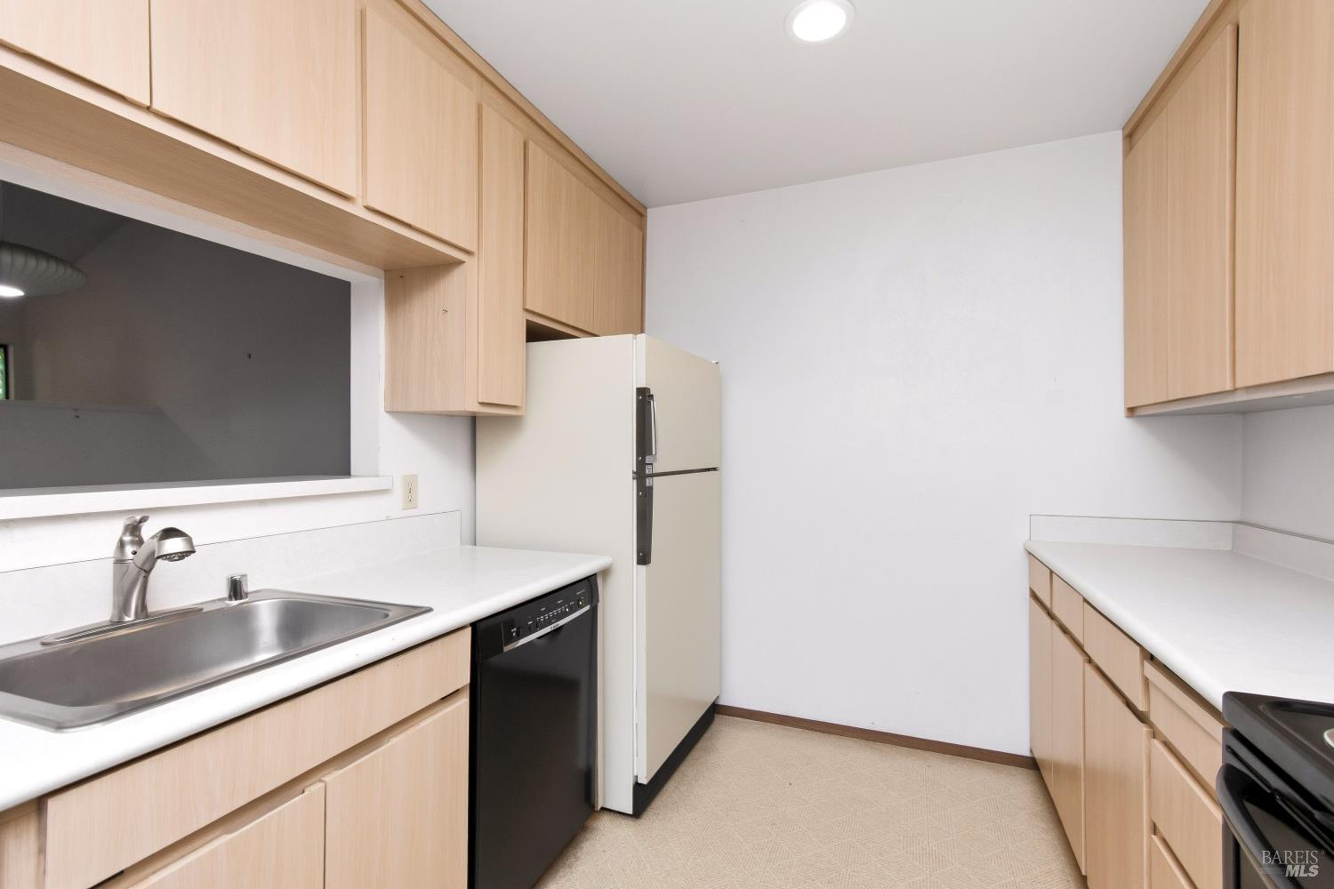 Kitchen with light wood cabinets, white countertops, and a stainless-steel sink.