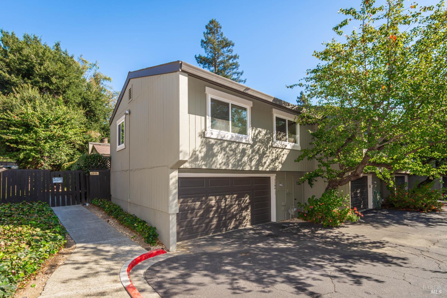 Gray two-story home with a double garage and leafy trees shading the driveway.