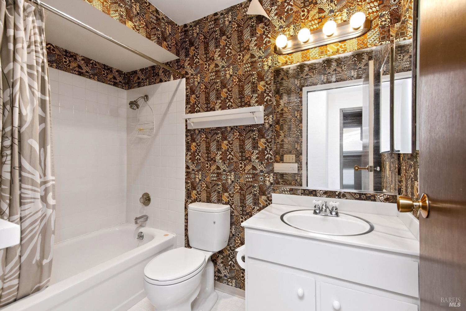 Bathroom with a white tub and vanity, large mirror, and bold brown-and-gold patterned tile.