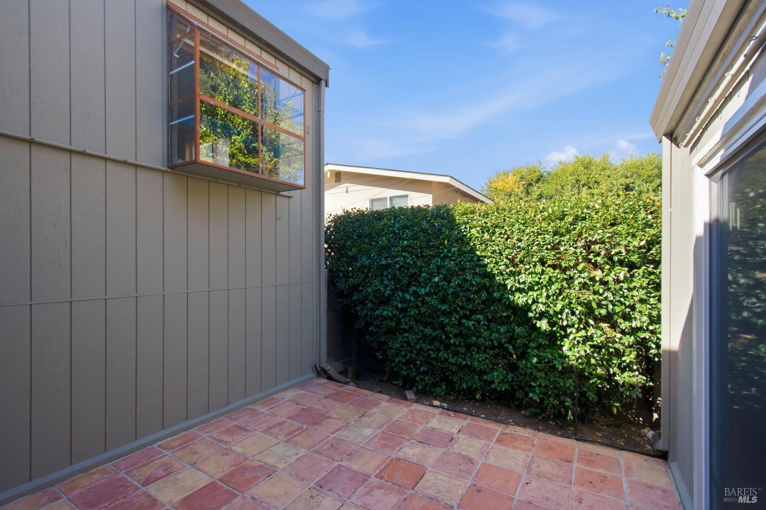 Tiled patio between gray-sided walls, bordered by a tall green hedge.
