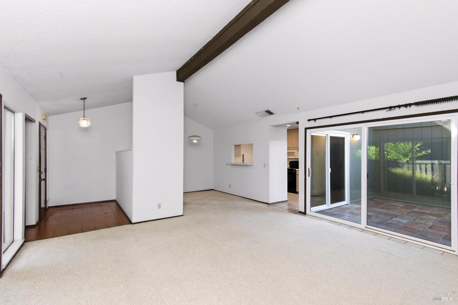 Unfurnished living room with a dark ceiling beam and sliding glass doors to a brick patio.