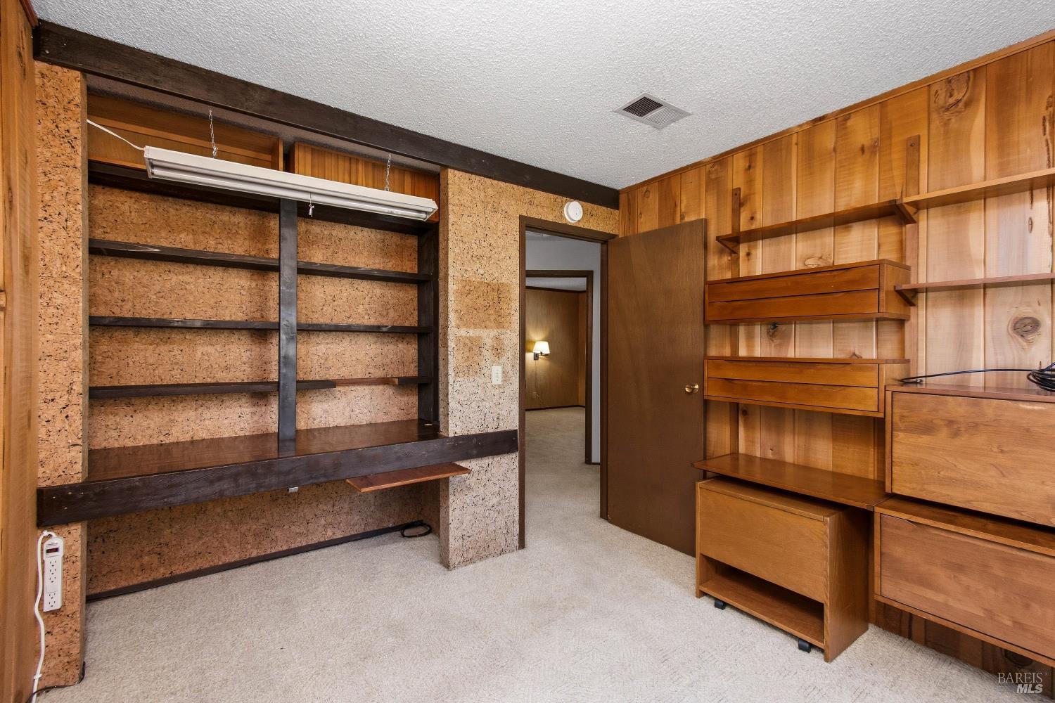 Room with extensive built-in wood shelving and drawers, wood-paneled walls, and light carpeting.
