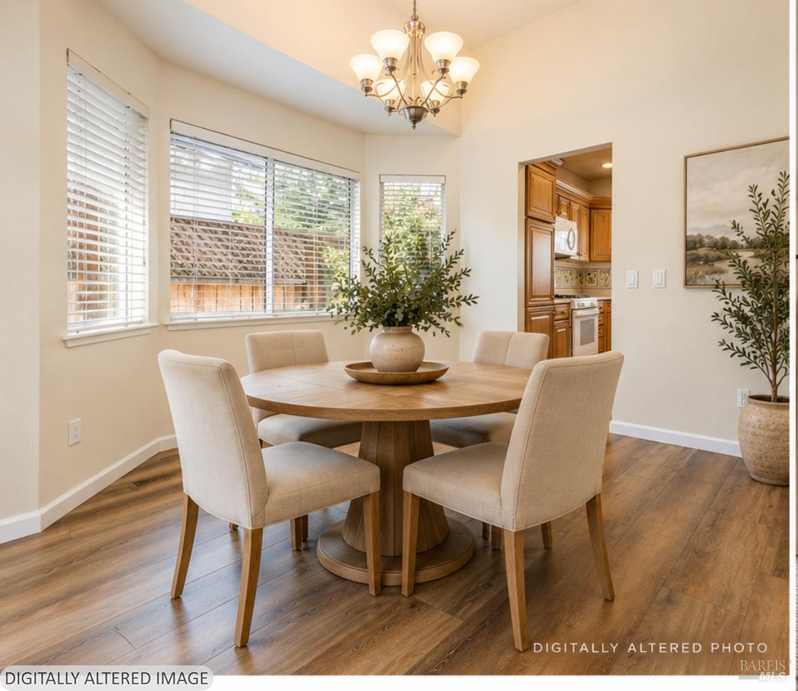 Dining room with a round wood table, upholstered chairs, chandelier, and windows overlooking a fenced yard.