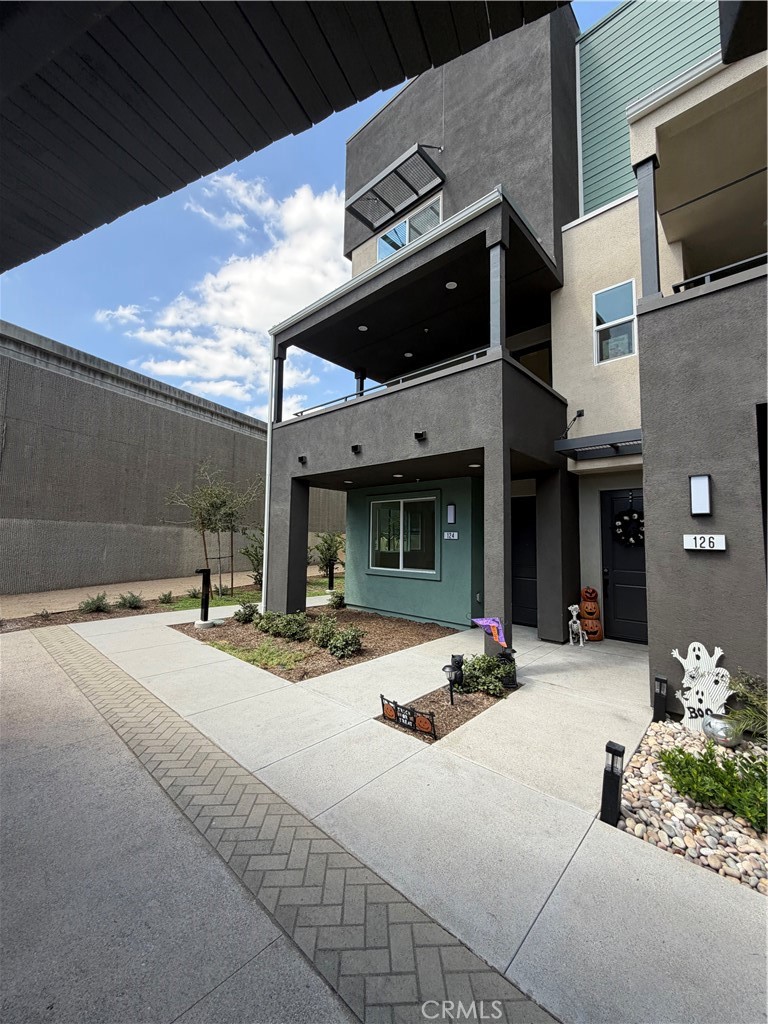 Modern gray townhouse entrance with a covered balcony, concrete walkway, and Halloween decorations.
