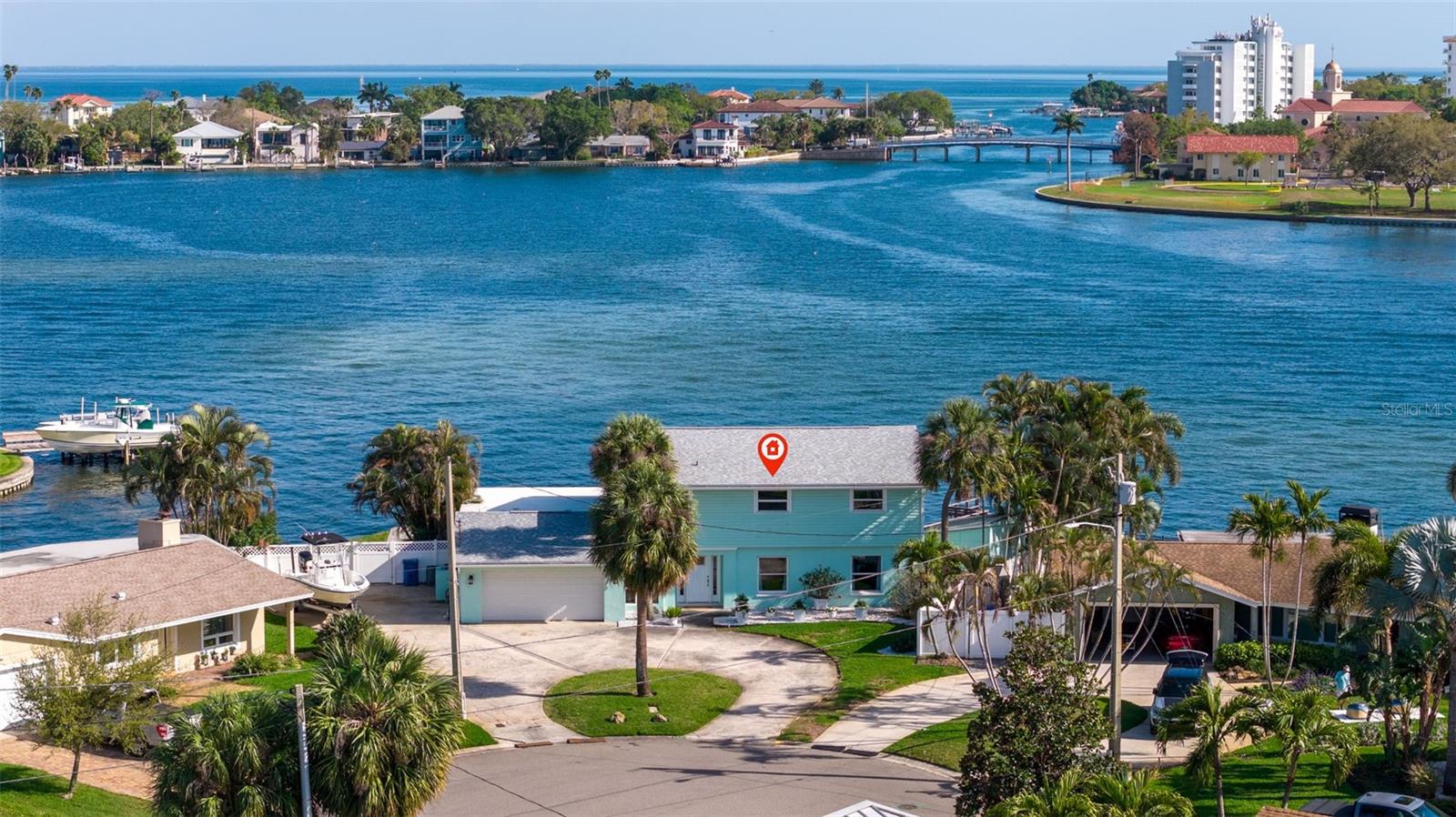 Aerial view of a turquoise waterfront home beside a bay, bridge, and neighboring homes.