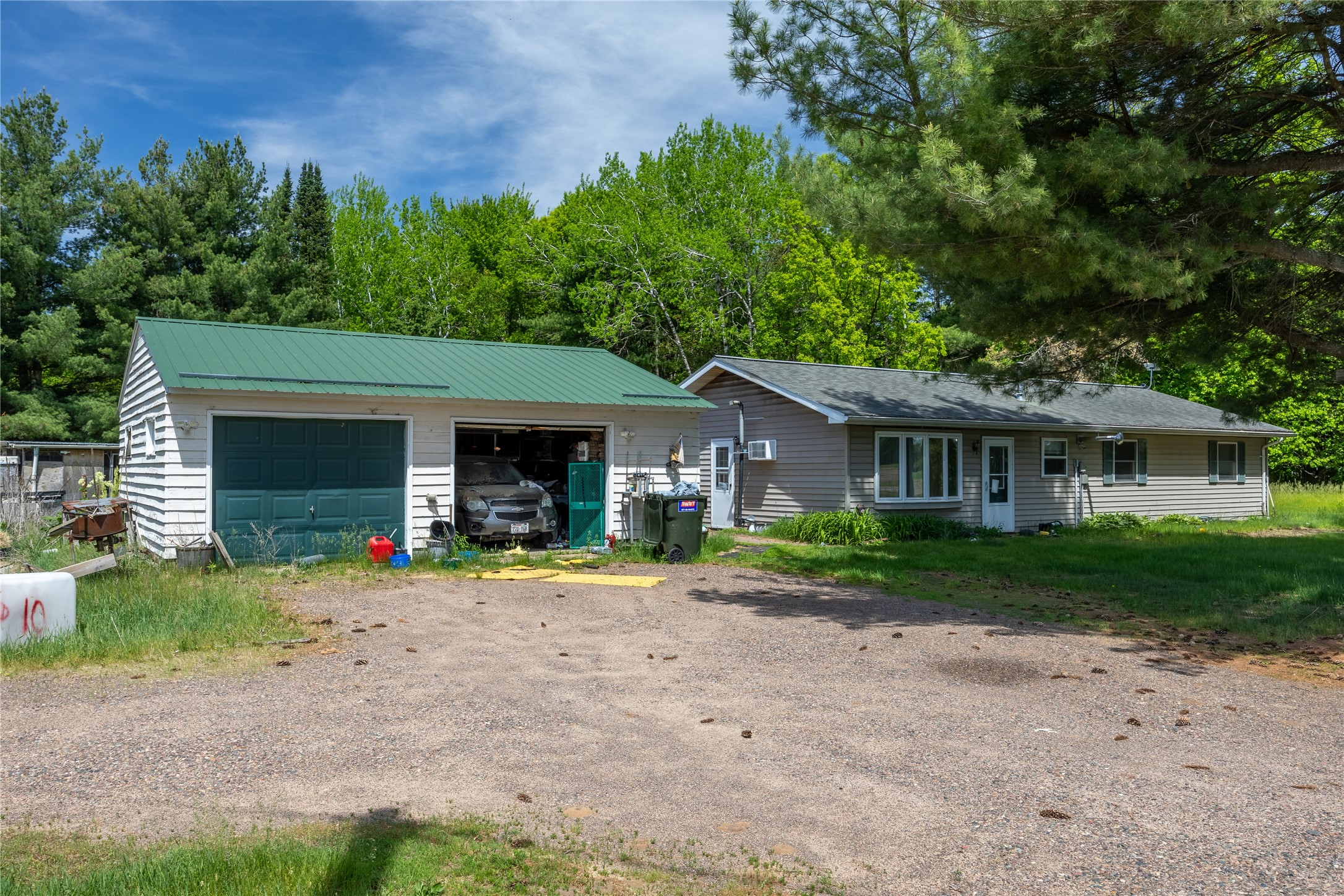 Single-story home beside a detached garage with a green metal roof and gravel driveway.