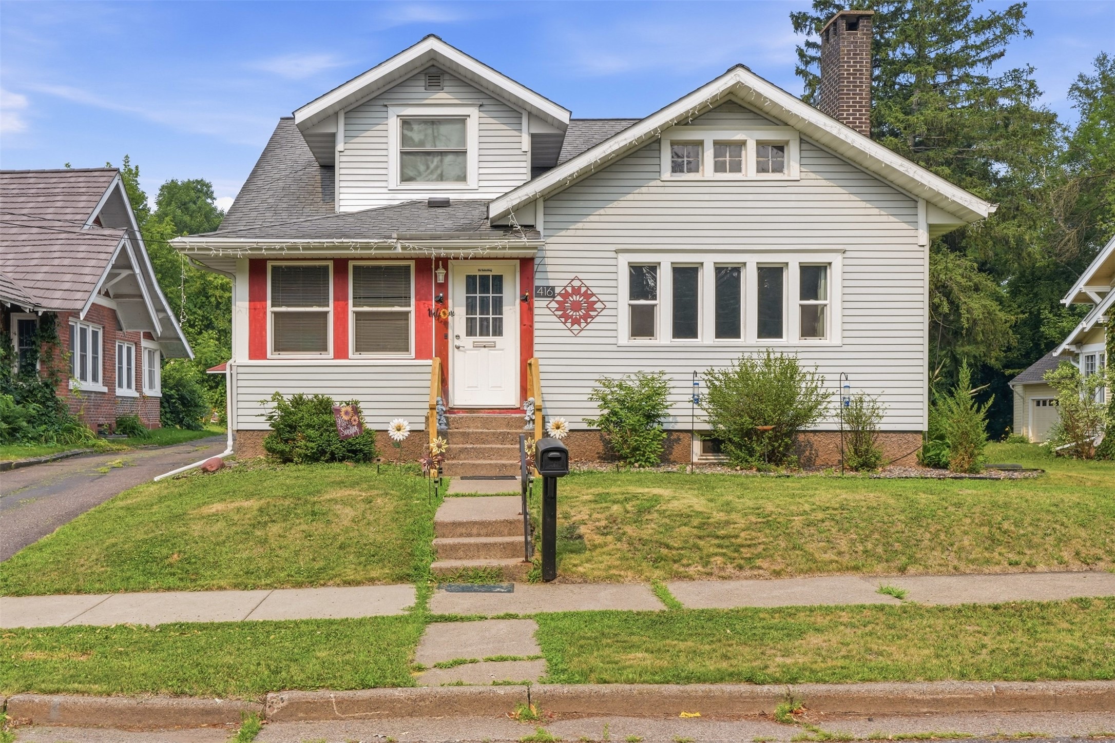 White-sided two-story home with a red entry, front dormer, brick chimney, and lawn.