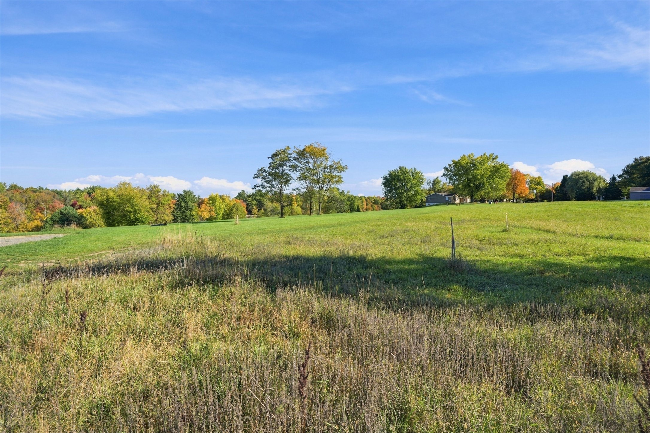 Open grassy acreage with autumn trees and homes along the distant edge.