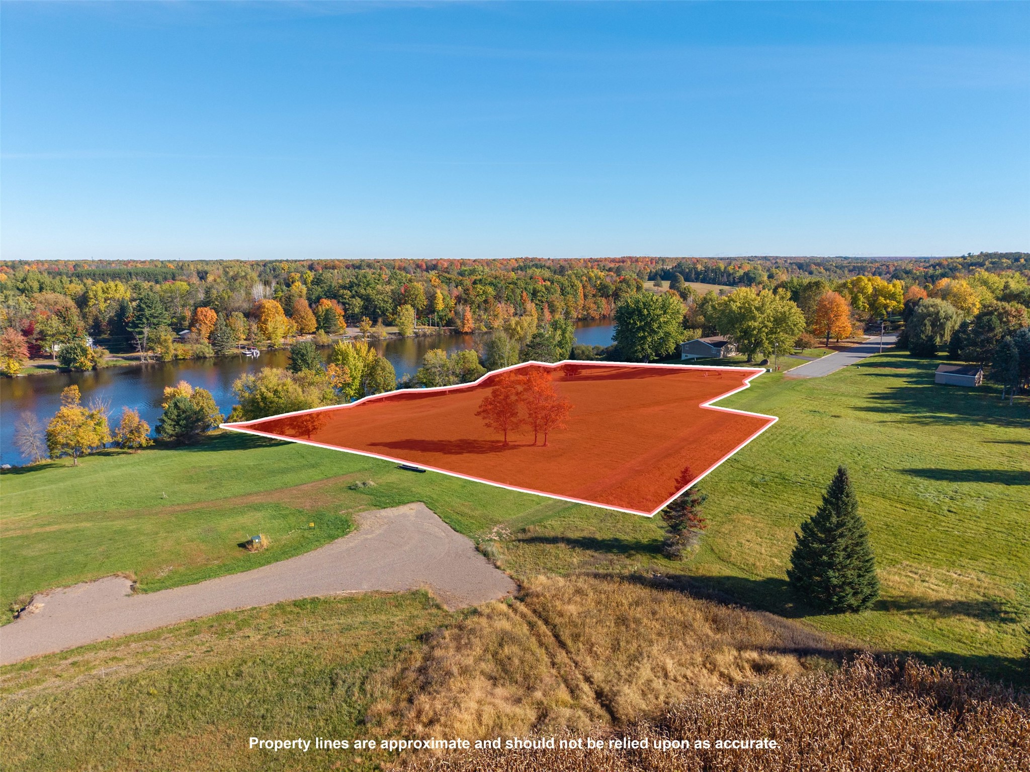 Aerial view of vacant land outlined beside a river, surrounded by autumn-colored trees.