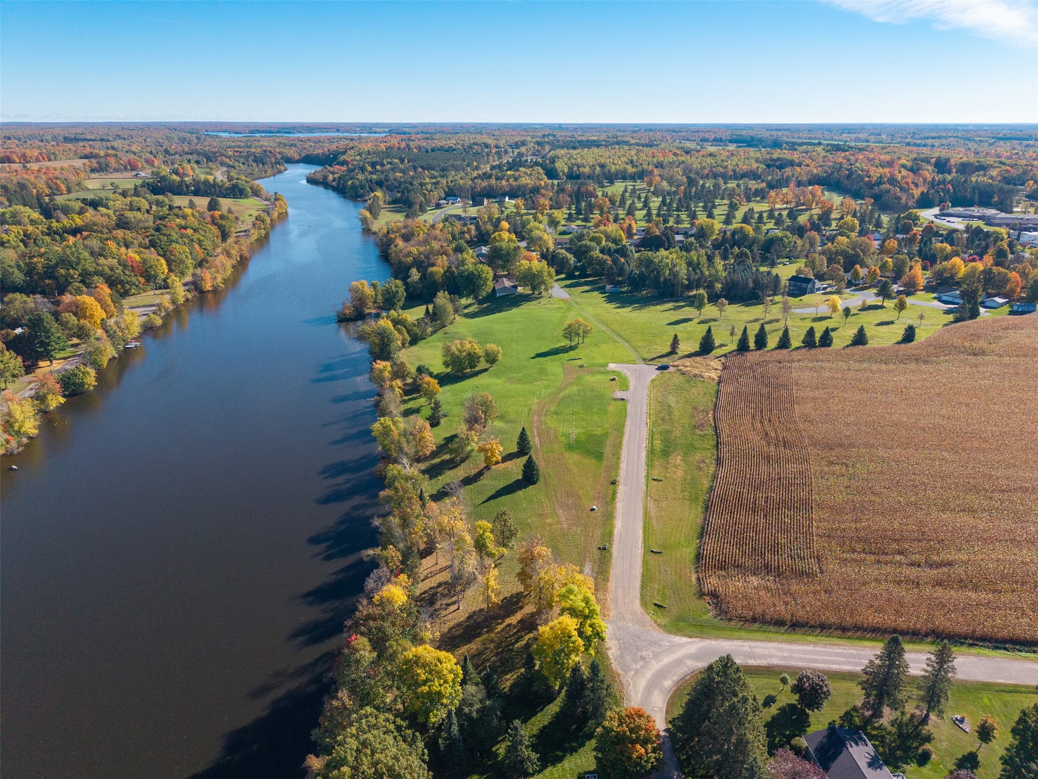 Aerial view of a river winding past autumn-colored homes, open lawns, and a cultivated field.