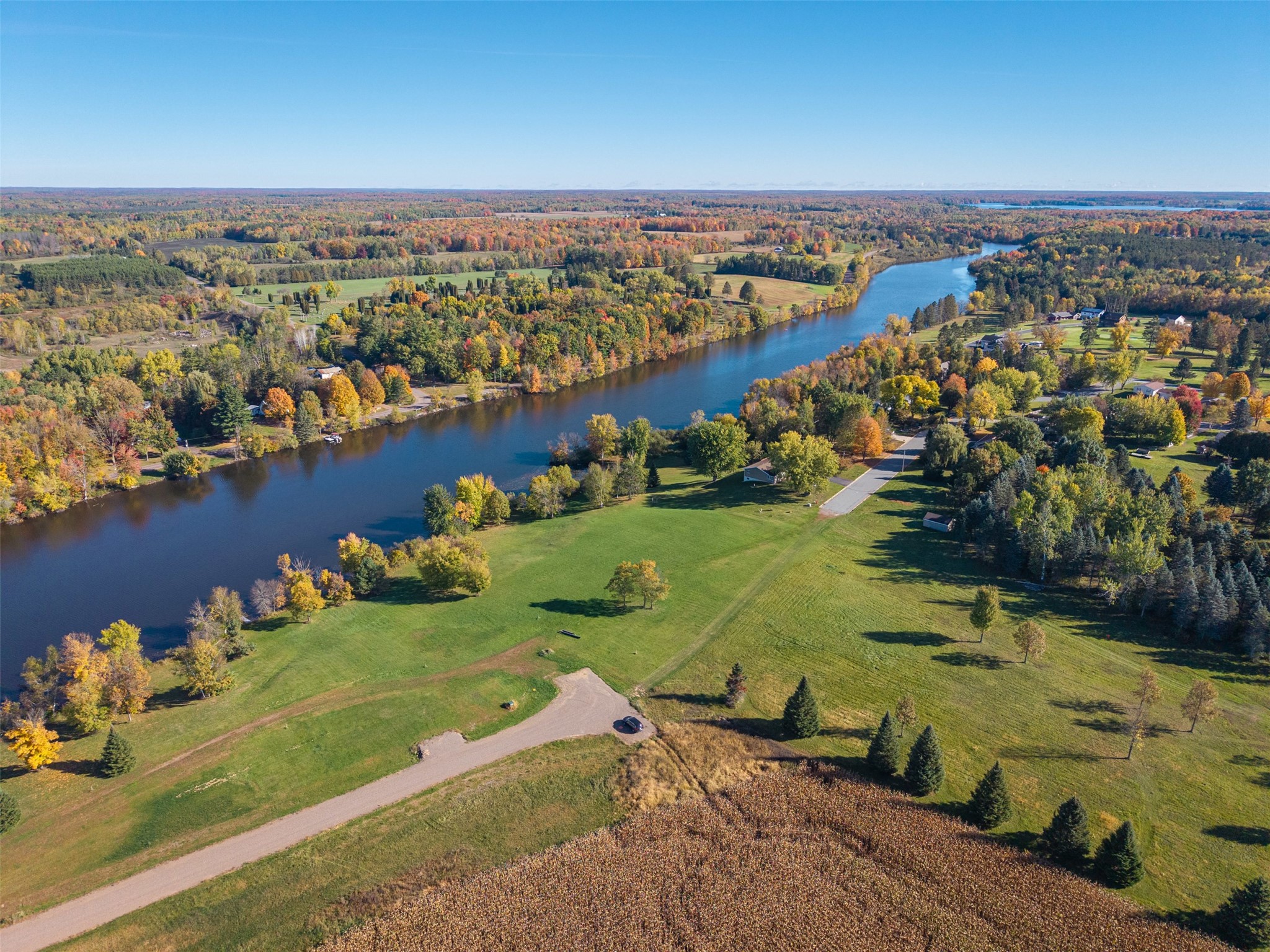Aerial view of grassy land beside a winding river, with autumn trees and a road nearby.