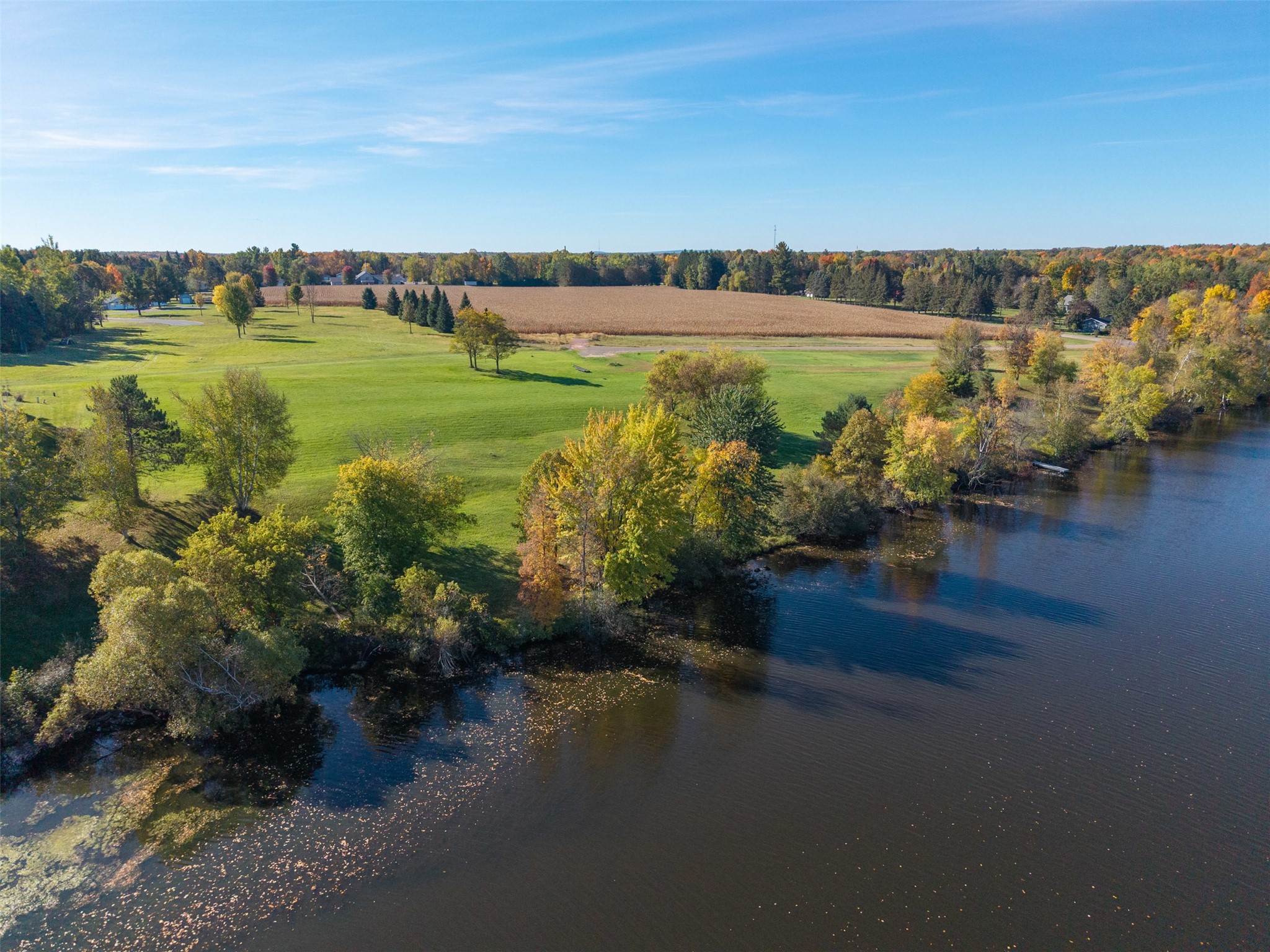Aerial view of grassy acreage beside a lake, with autumn trees and fields beyond.