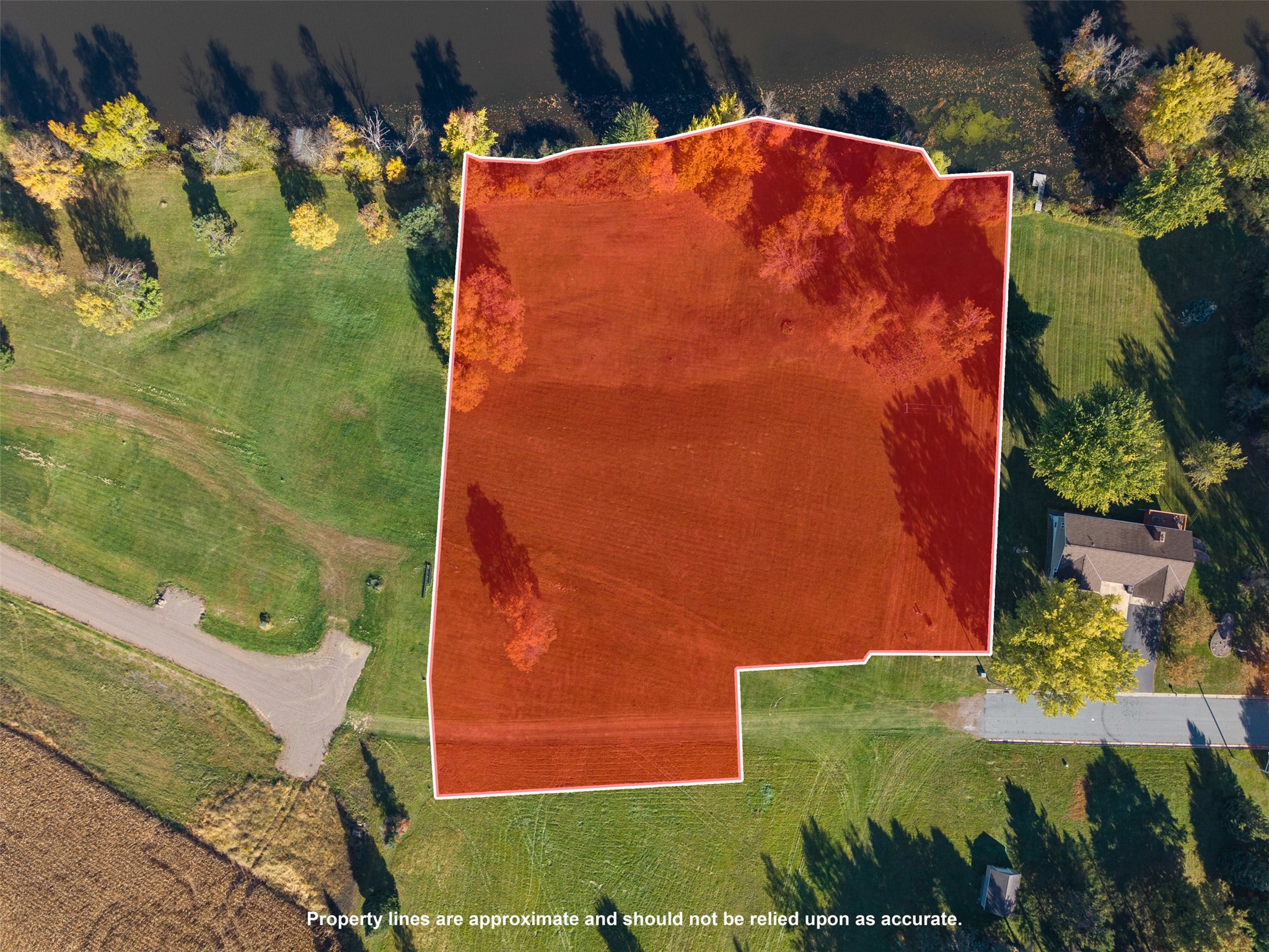 Aerial view of a grassy parcel outlined in red and white, surrounded by trees and neighboring properties.