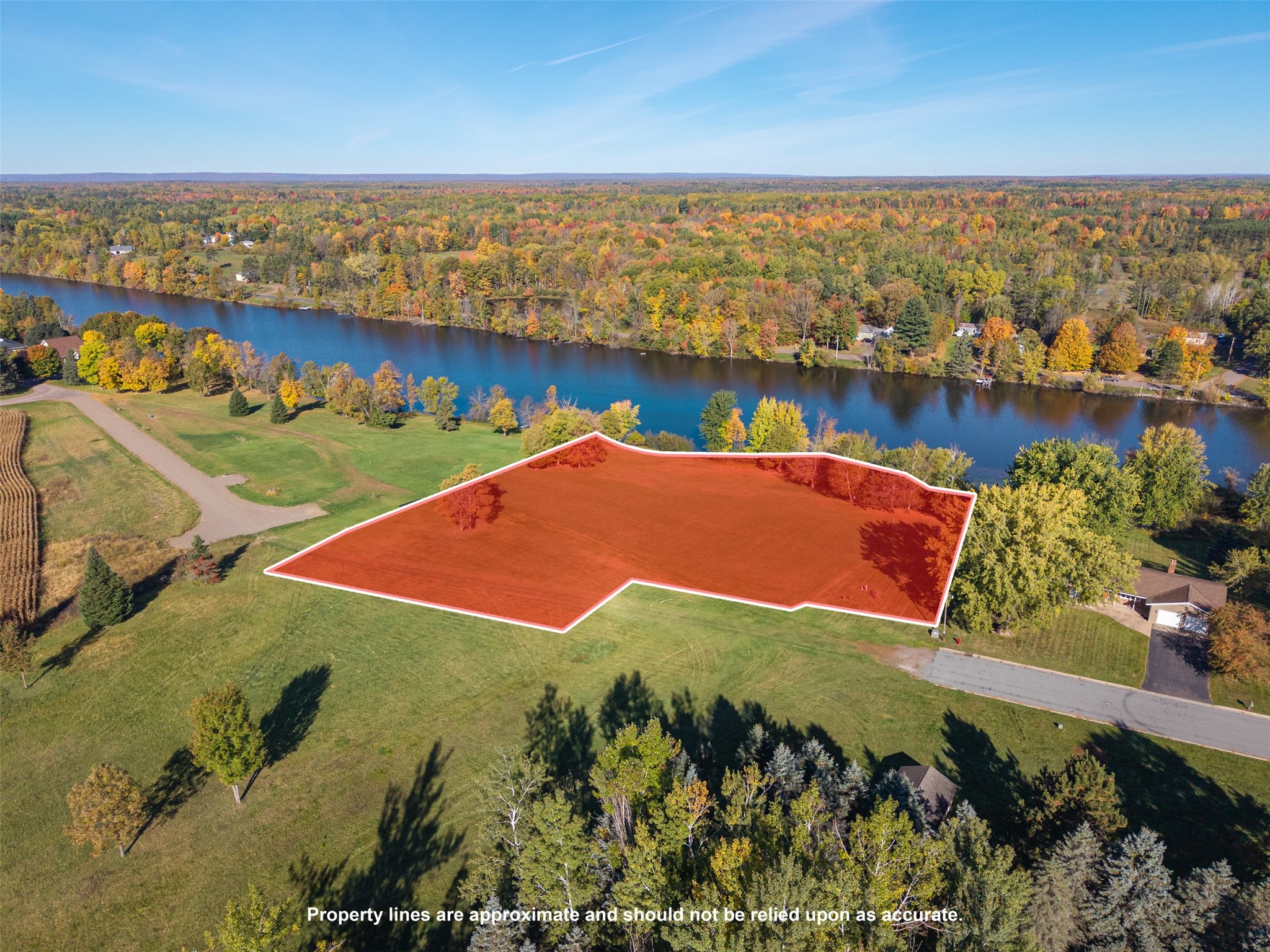 Aerial view of a riverfront land parcel outlined in red, with autumn trees and road access.