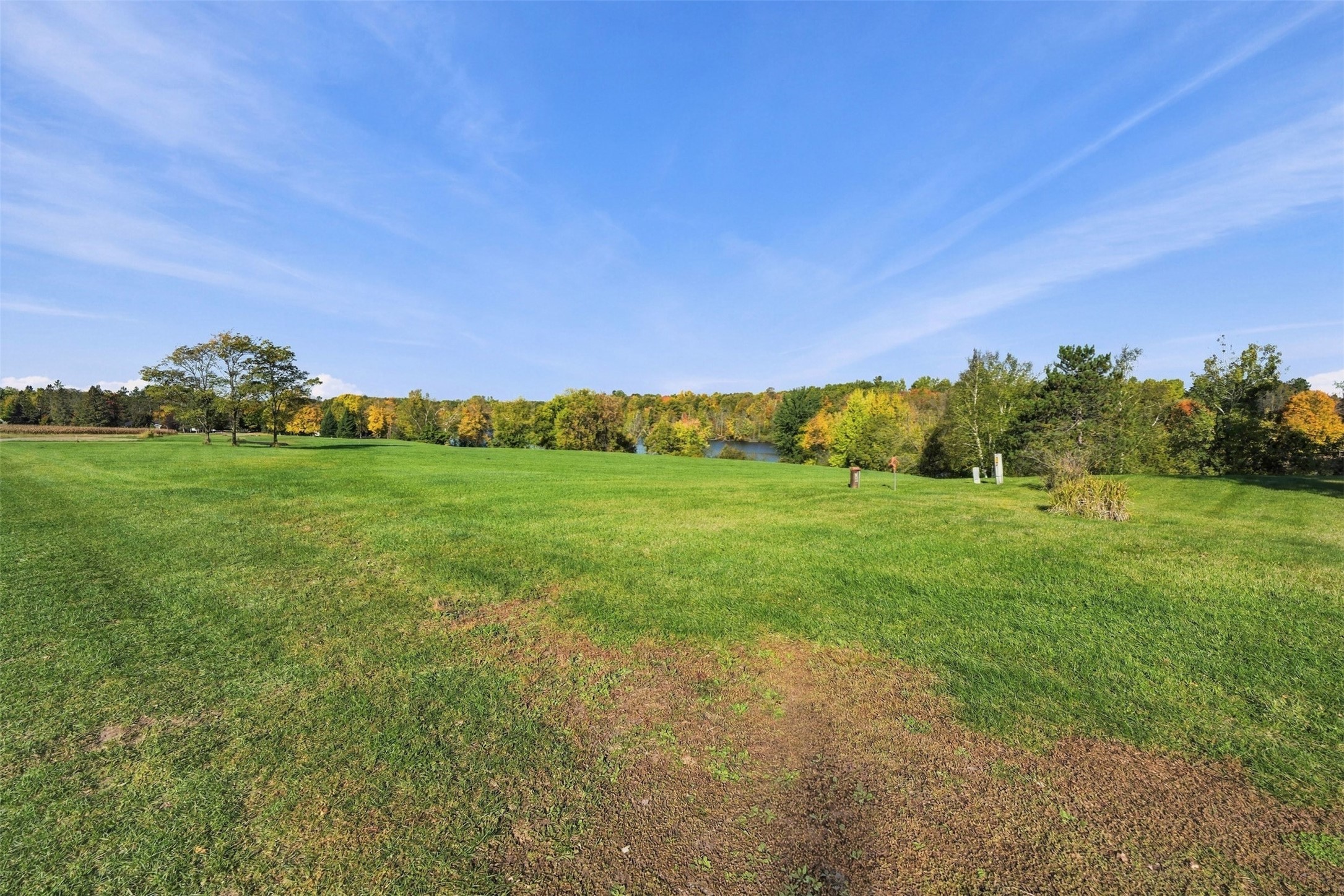 Open grassy lot with a distant lake and autumn-colored trees along the horizon.