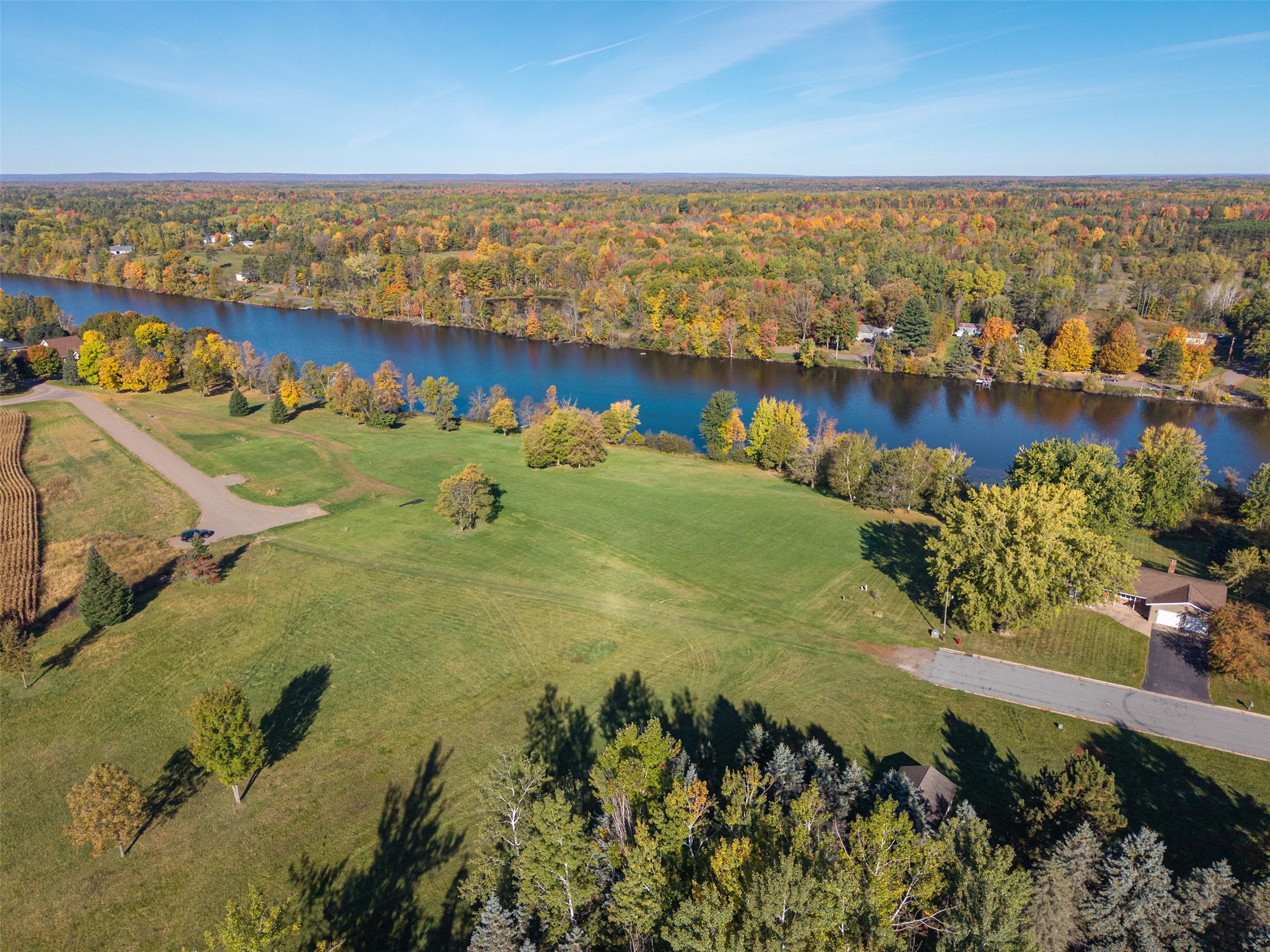 Aerial view of grassy acreage along a river, with autumn trees lining the far bank.