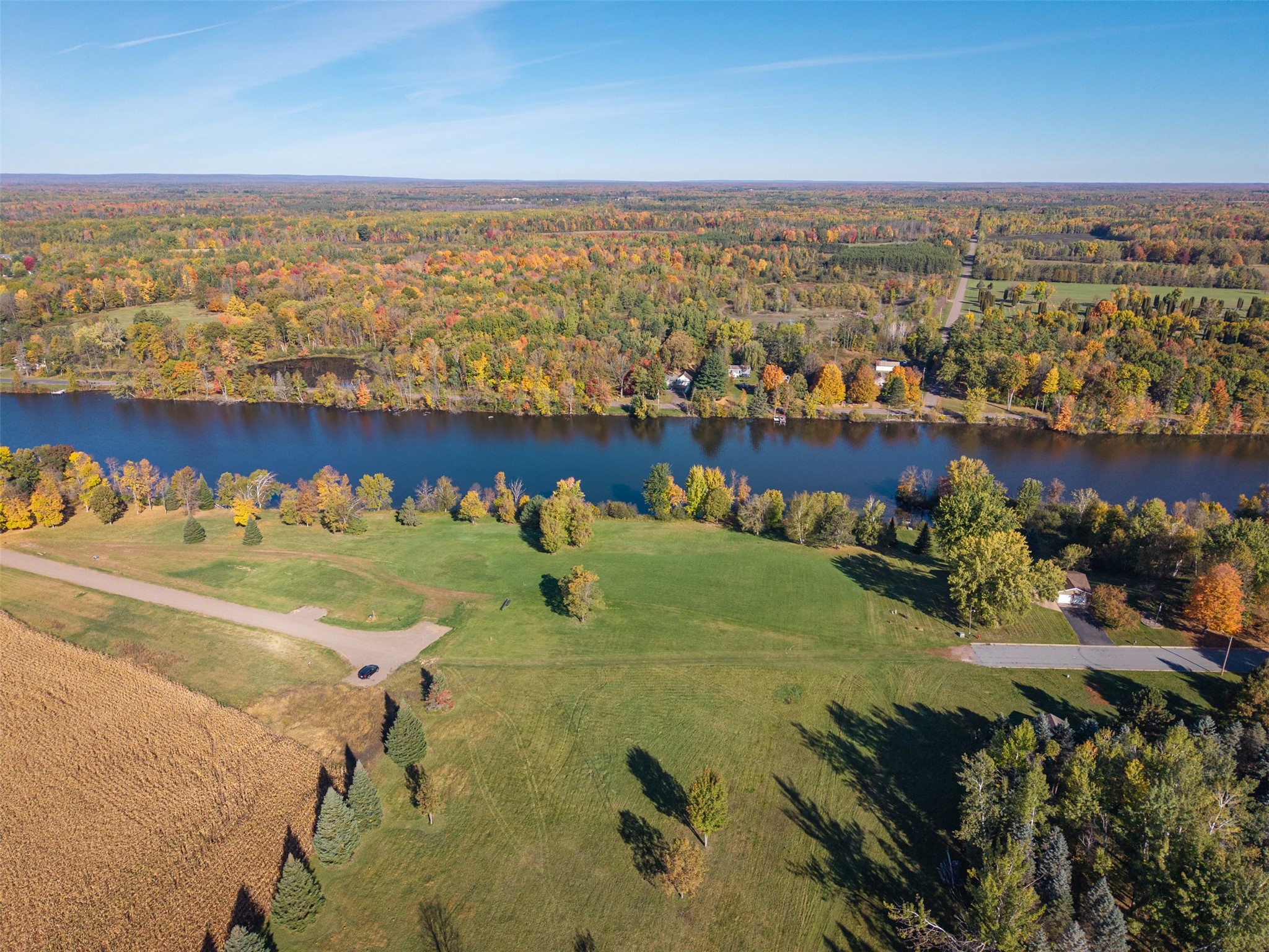 Aerial view of grassy acreage along a river, with scattered trees and a cornfield.