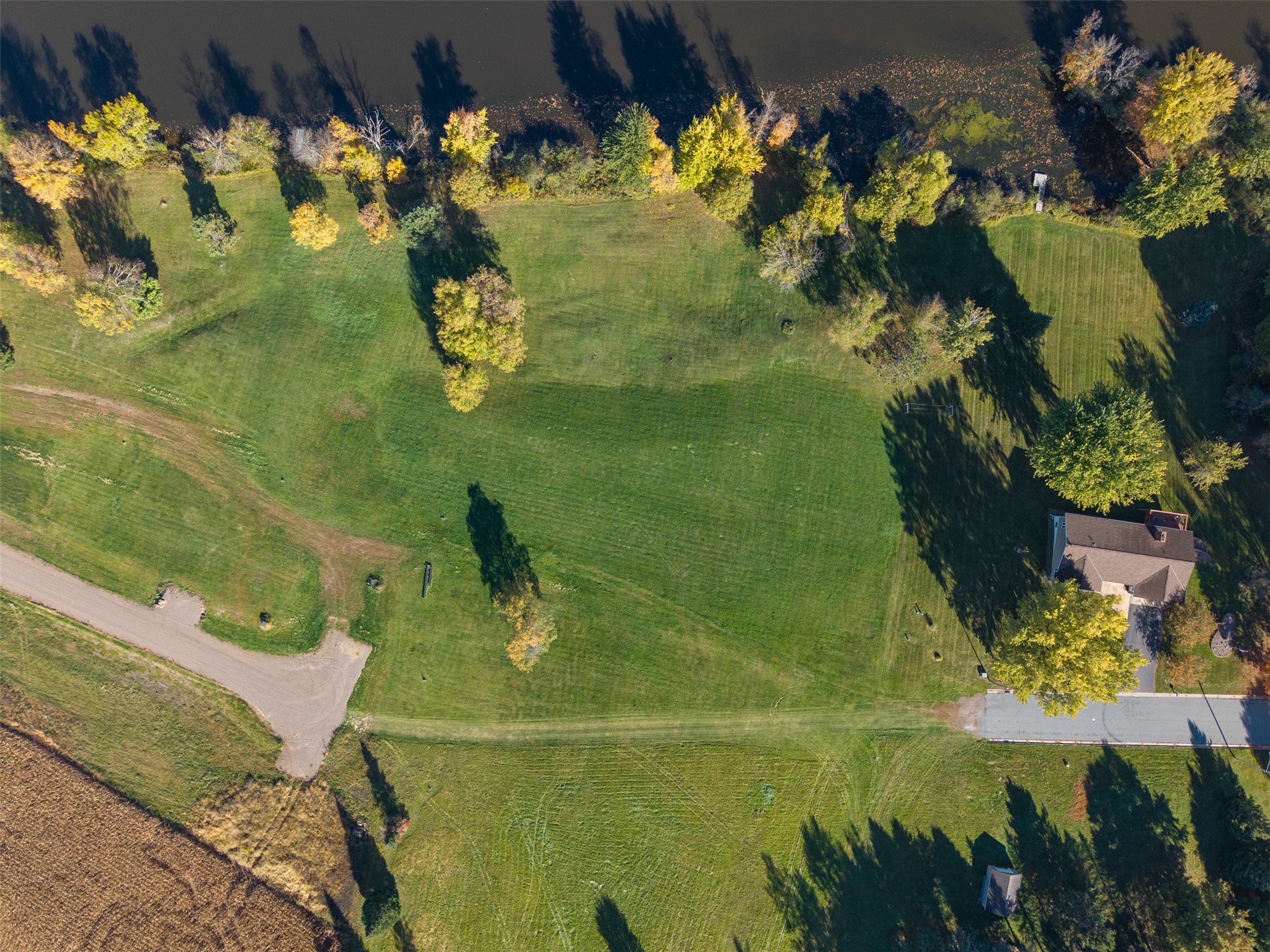 Aerial view of a grassy property bordered by autumn trees and water.