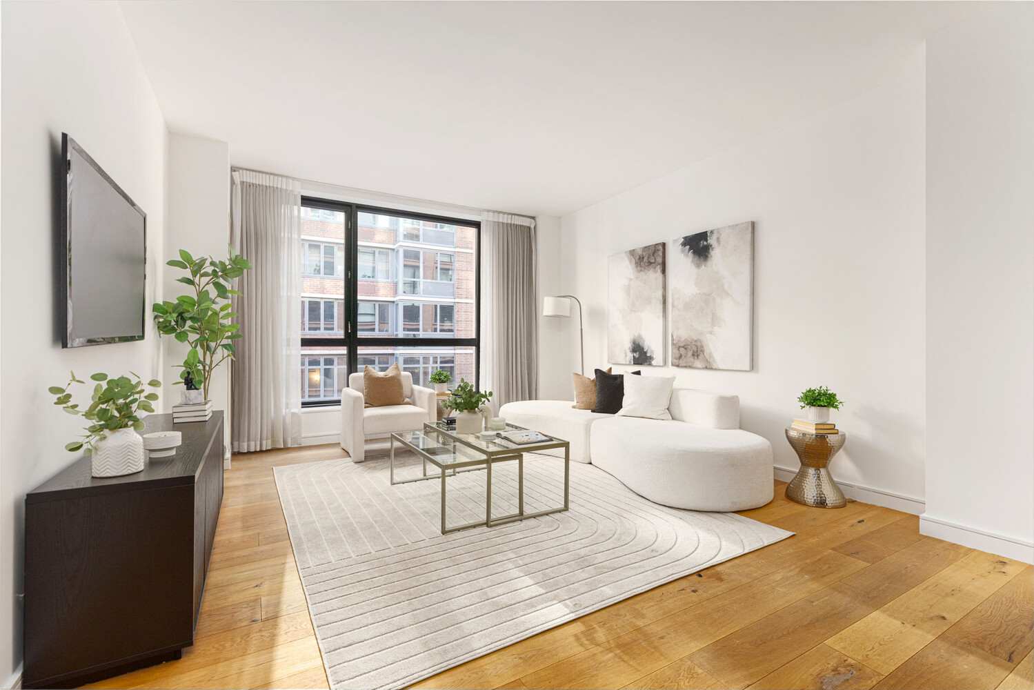 Furnished living room with white seating, warm wood floors, and large windows overlooking neighboring buildings.