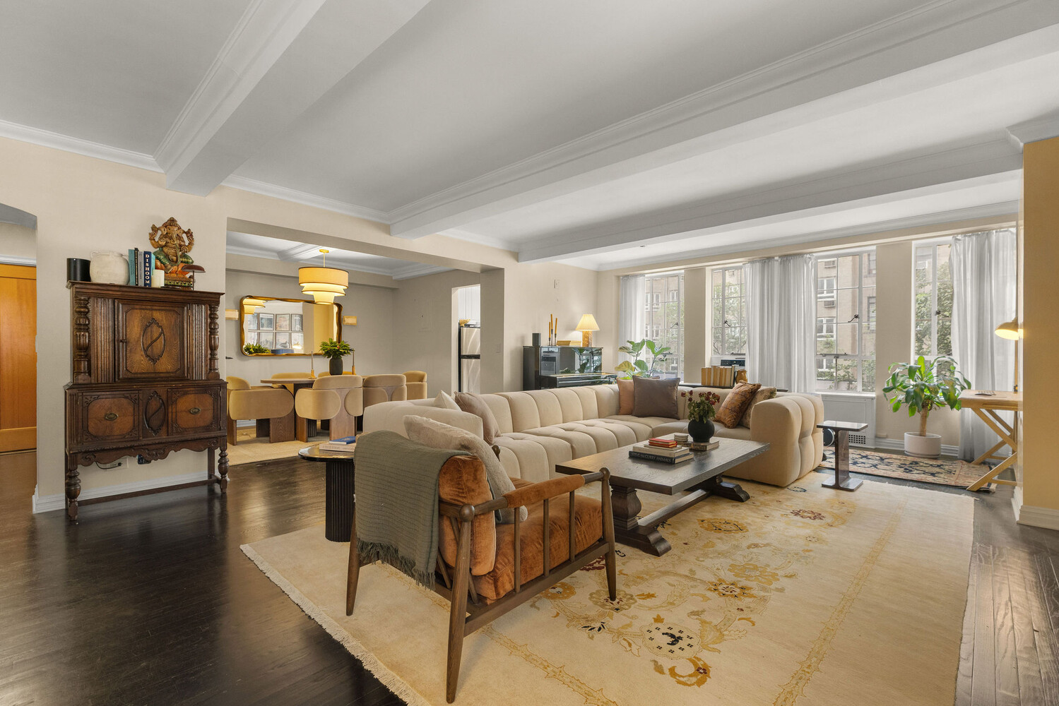 Furnished living room with a cream sectional, patterned rug, dark hardwood floors, and large curtained windows.