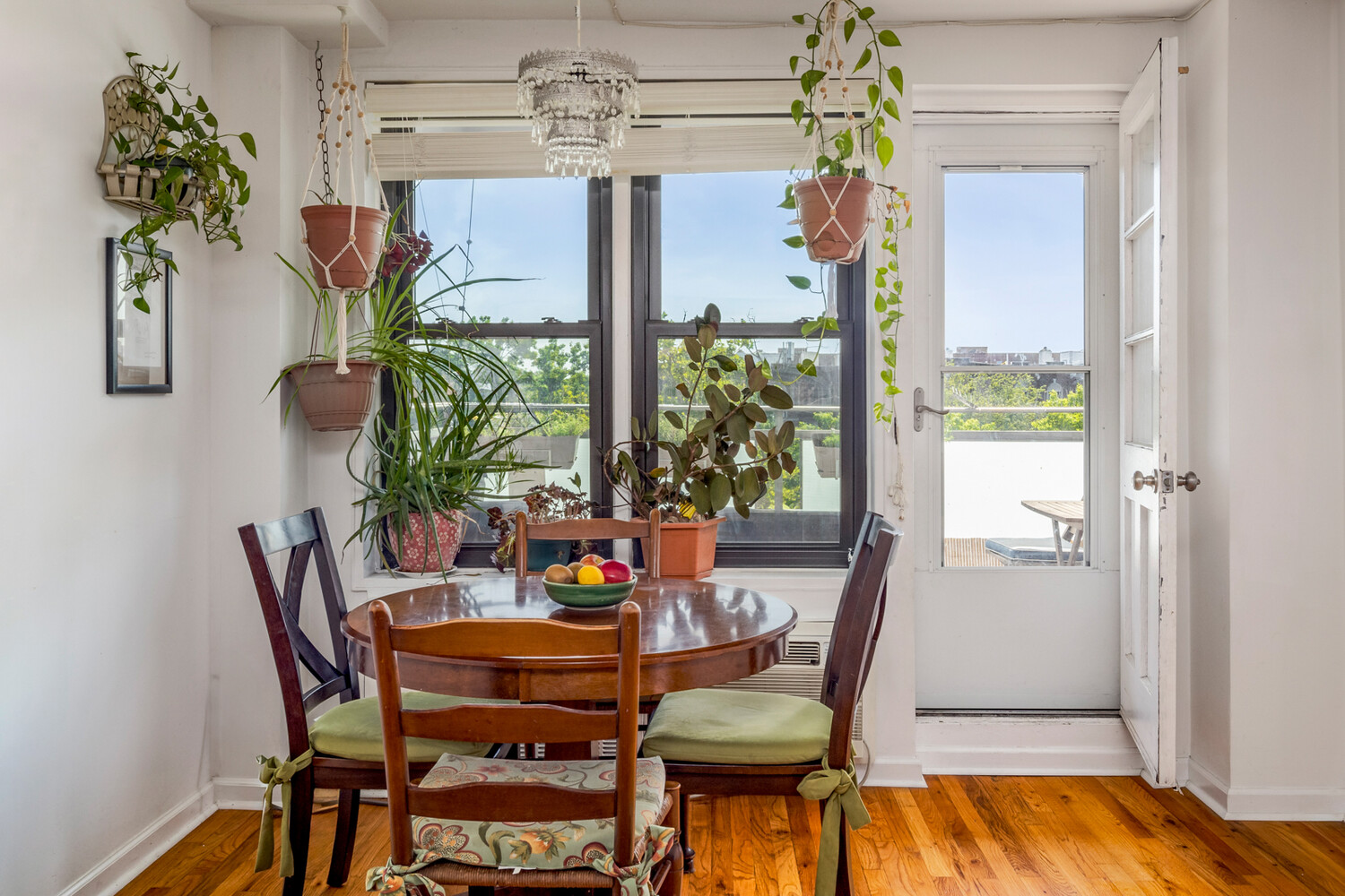Dining area with a round wooden table, hanging plants, and a glass door to the terrace.