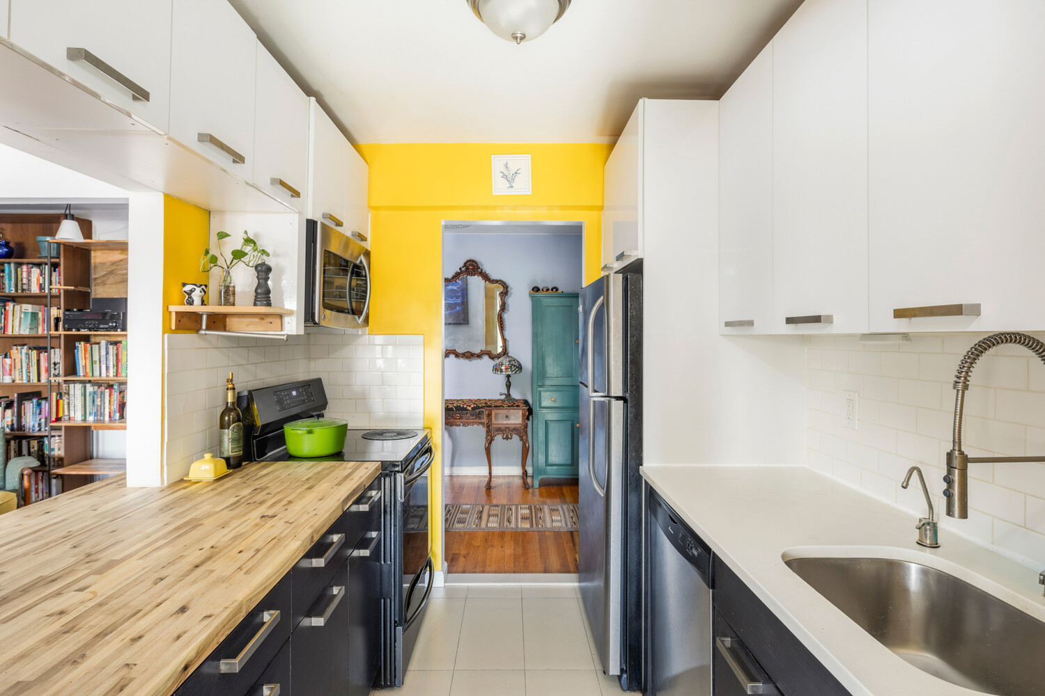 Apartment kitchen with butcher-block counter, stainless steel appliances, and a bright yellow doorway wall.