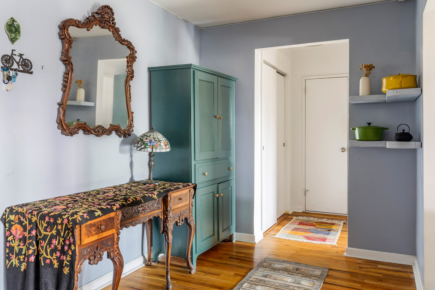 Apartment entryway with an ornate wooden console, teal cabinet, and polished hardwood floors.
