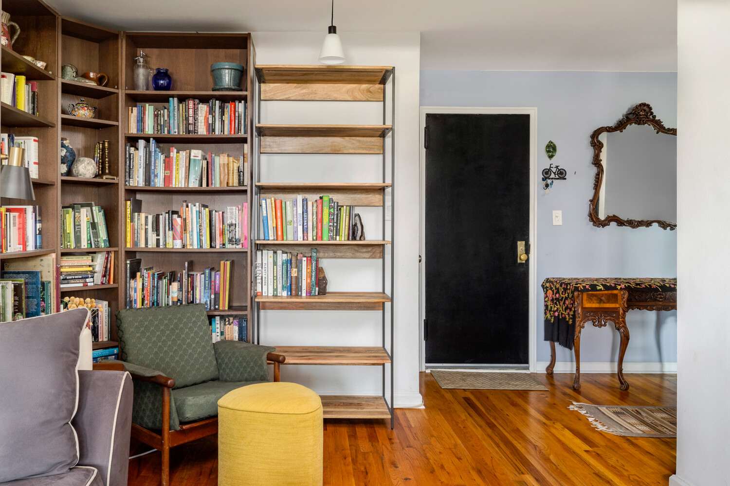 Living room with tall wooden bookshelves, a green armchair, and a yellow ottoman.