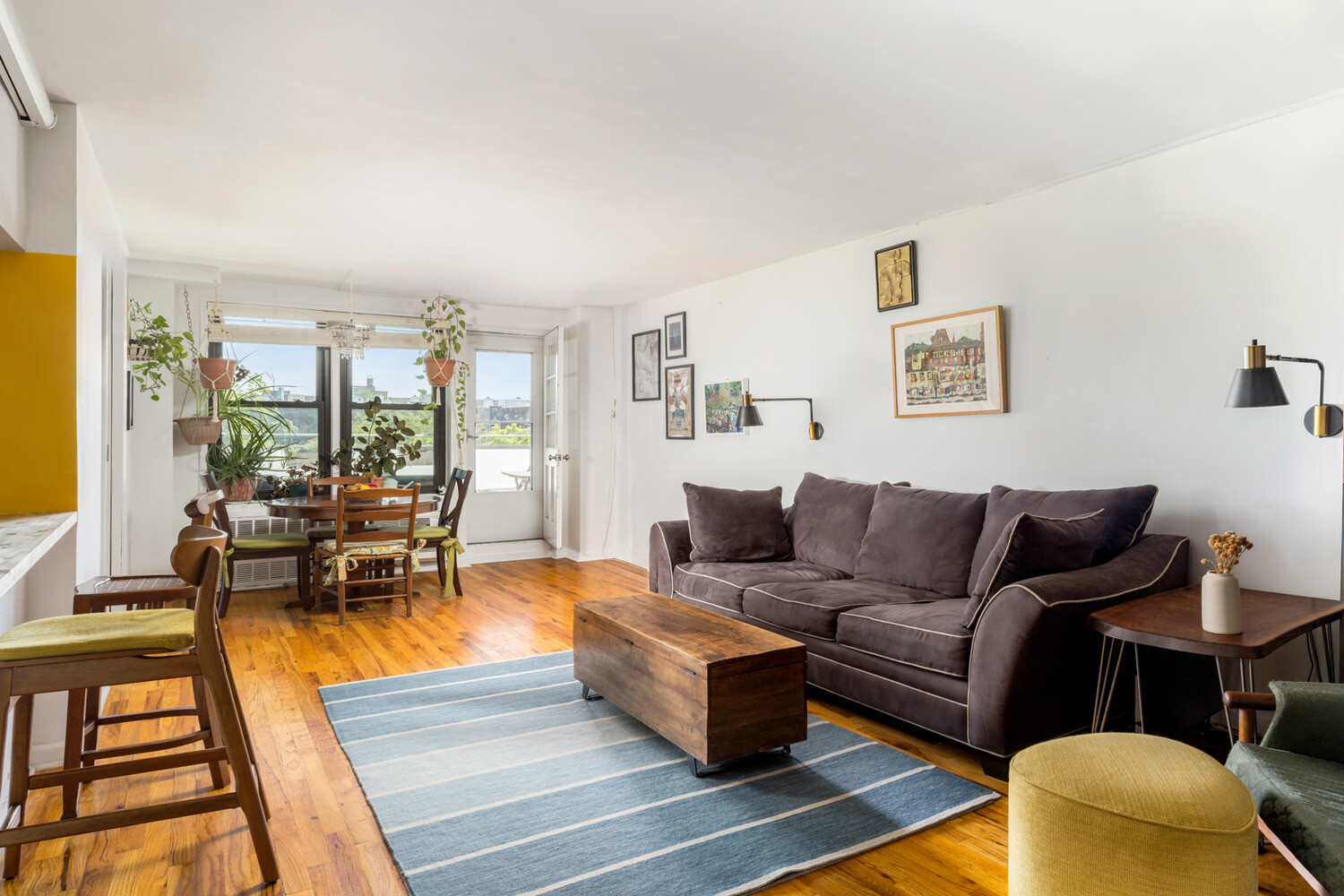 Apartment living and dining area with hardwood floors, large windows, and a dark gray sofa.