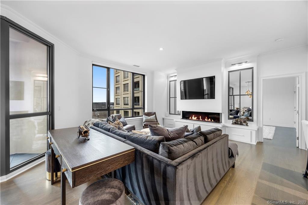 Furnished living room with a sectional sofa, linear fireplace, and large windows overlooking a neighboring building.