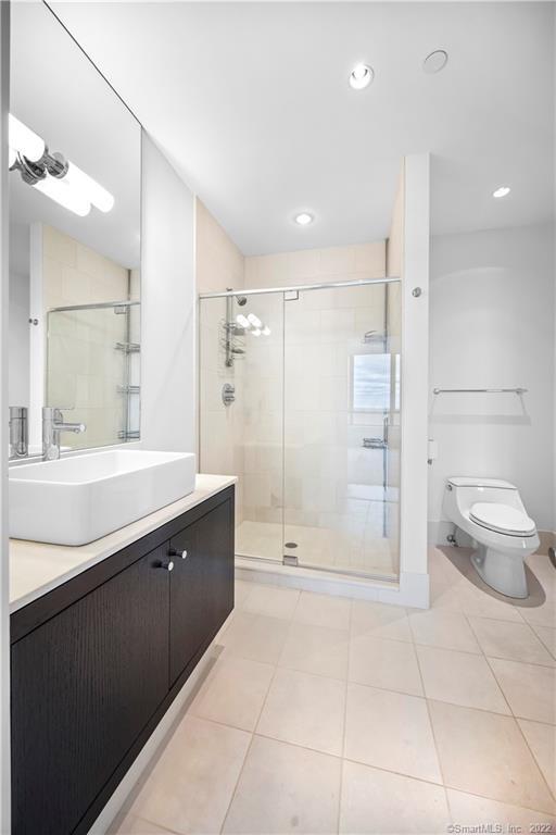 Bright bathroom with a glass-enclosed shower, pale tile, dark vanity, and white vessel sink.