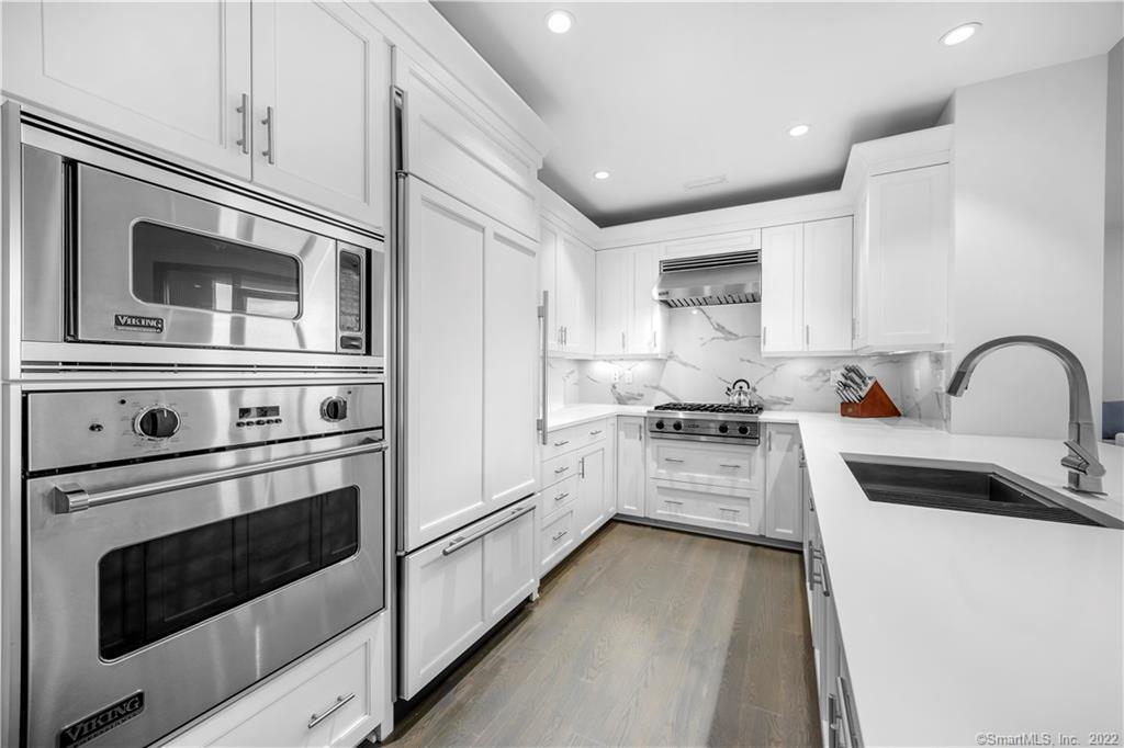 White kitchen with stainless Viking appliances, marble backsplash, and a peninsula sink.