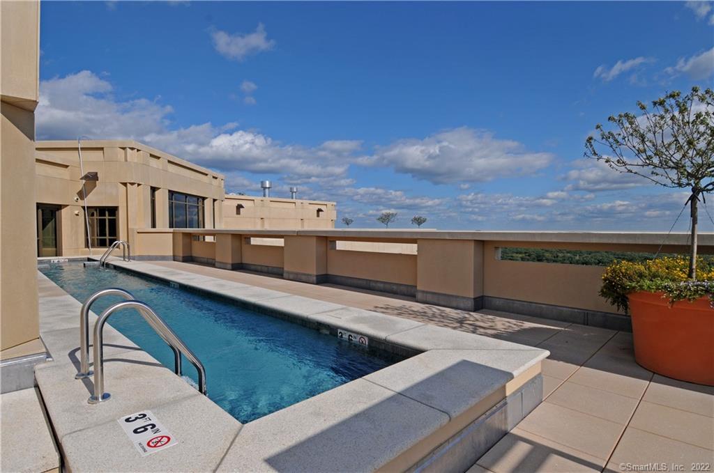 Rooftop swimming pool on a sunny terrace beside a modern beige building.