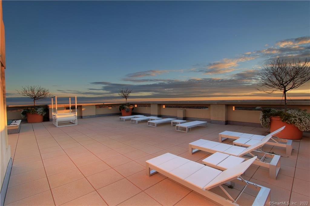 Rooftop terrace with lounge chairs and planters overlooking water at sunset.