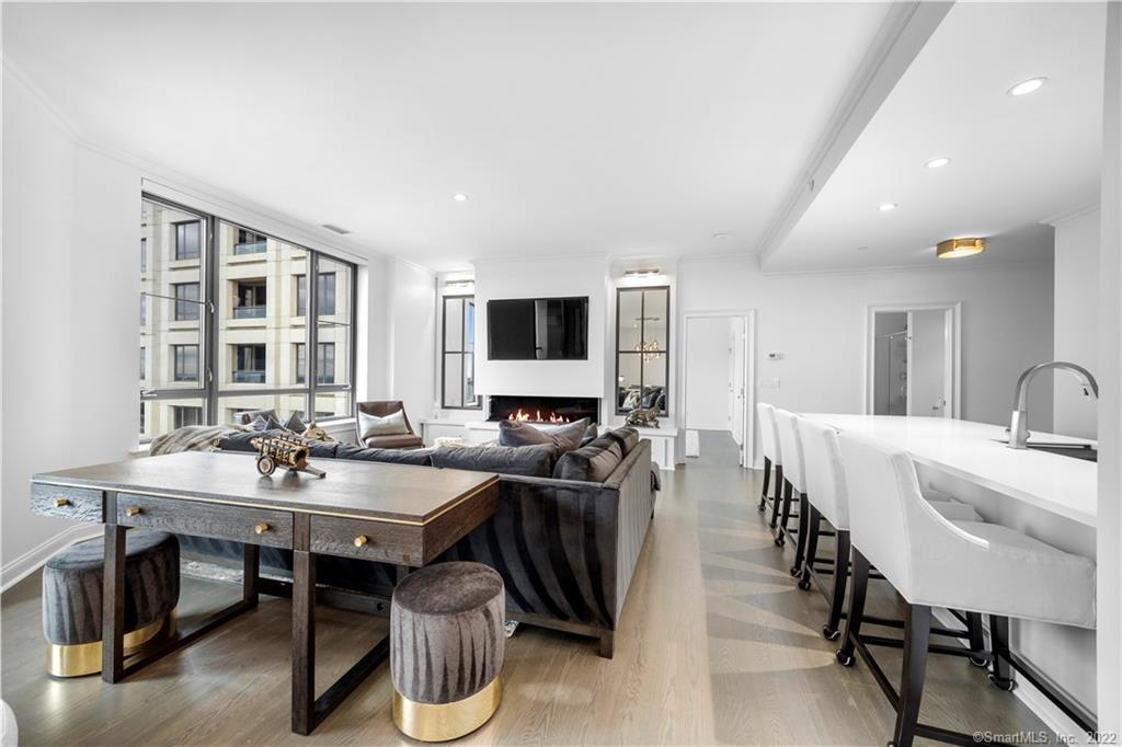Open-plan living room with a dark sectional, fireplace, large windows, and white kitchen island.