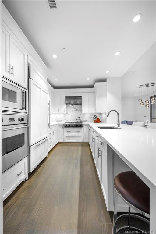 Modern white kitchen with stainless-steel ovens and a long island with sink.
