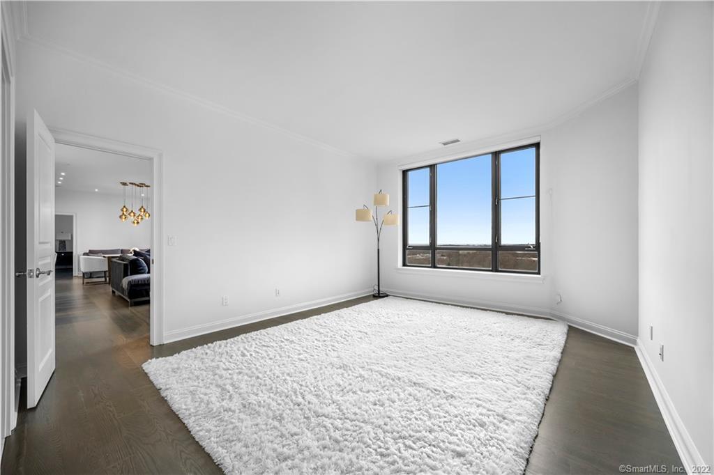 Bright bedroom with a large white rug, floor lamp, and wide window overlooking a distant horizon.