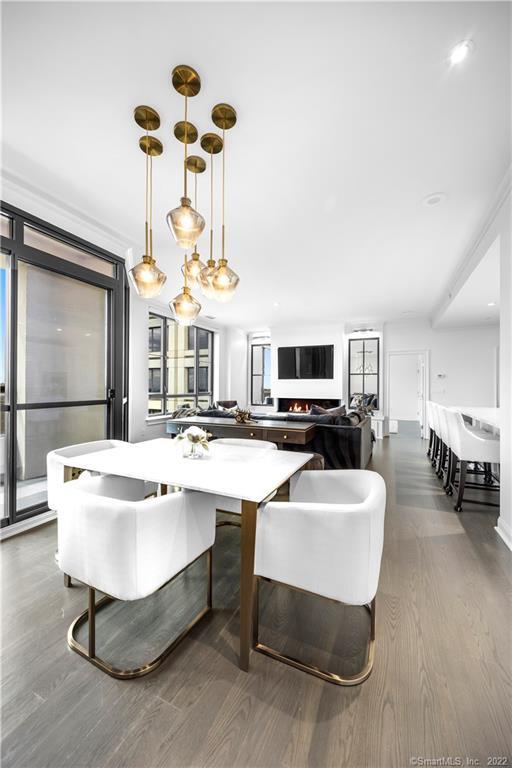 Open-plan condo dining and living area with white chairs, brass pendant lights, and a fireplace.