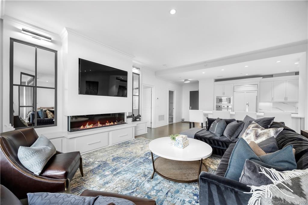 Furnished living room with a linear fireplace, wall-mounted television, and open kitchen.