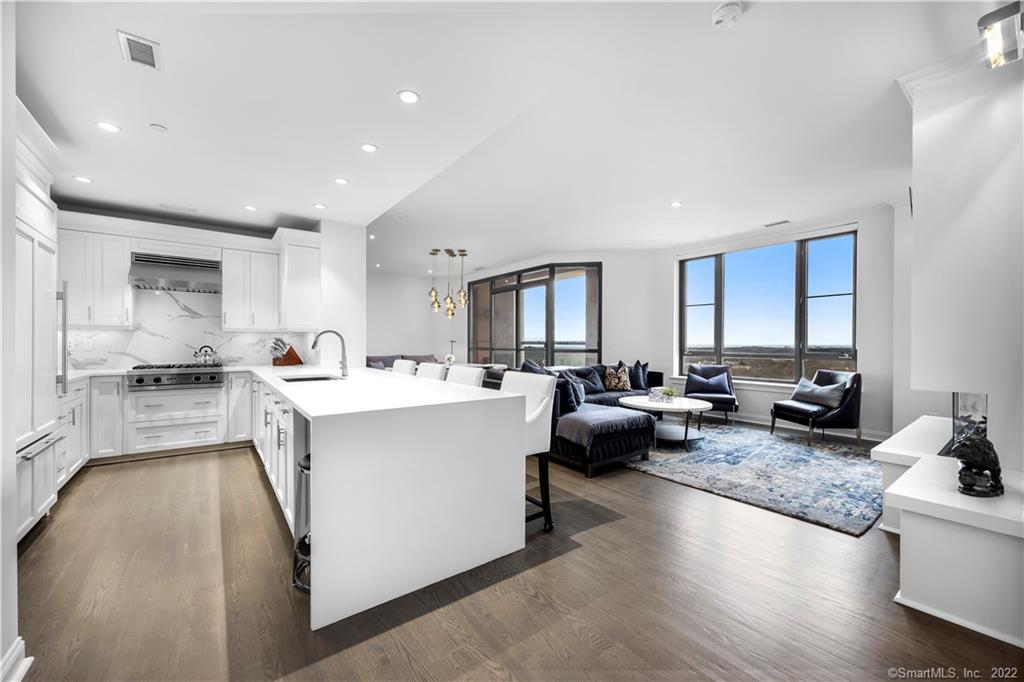 Open-plan kitchen and living room with a large white island, dark seating, and expansive windows.