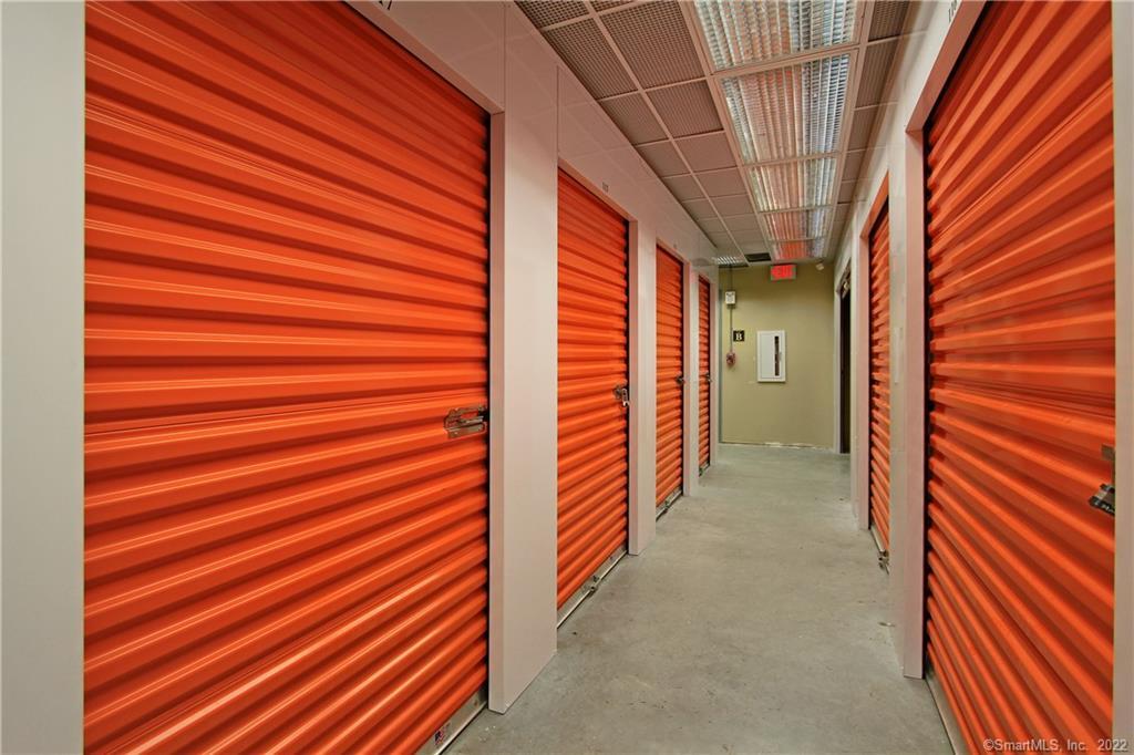 Storage facility hallway lined with bright orange roll-up doors and a concrete floor.